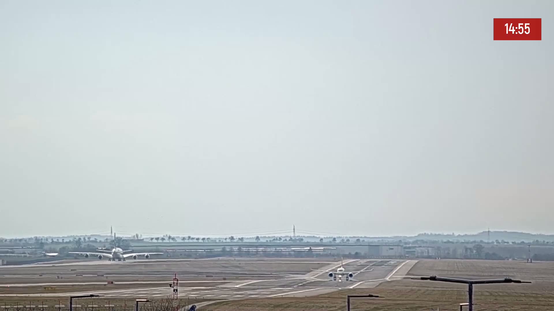 Two airplanes are on a runway at an airport on a hazy day.