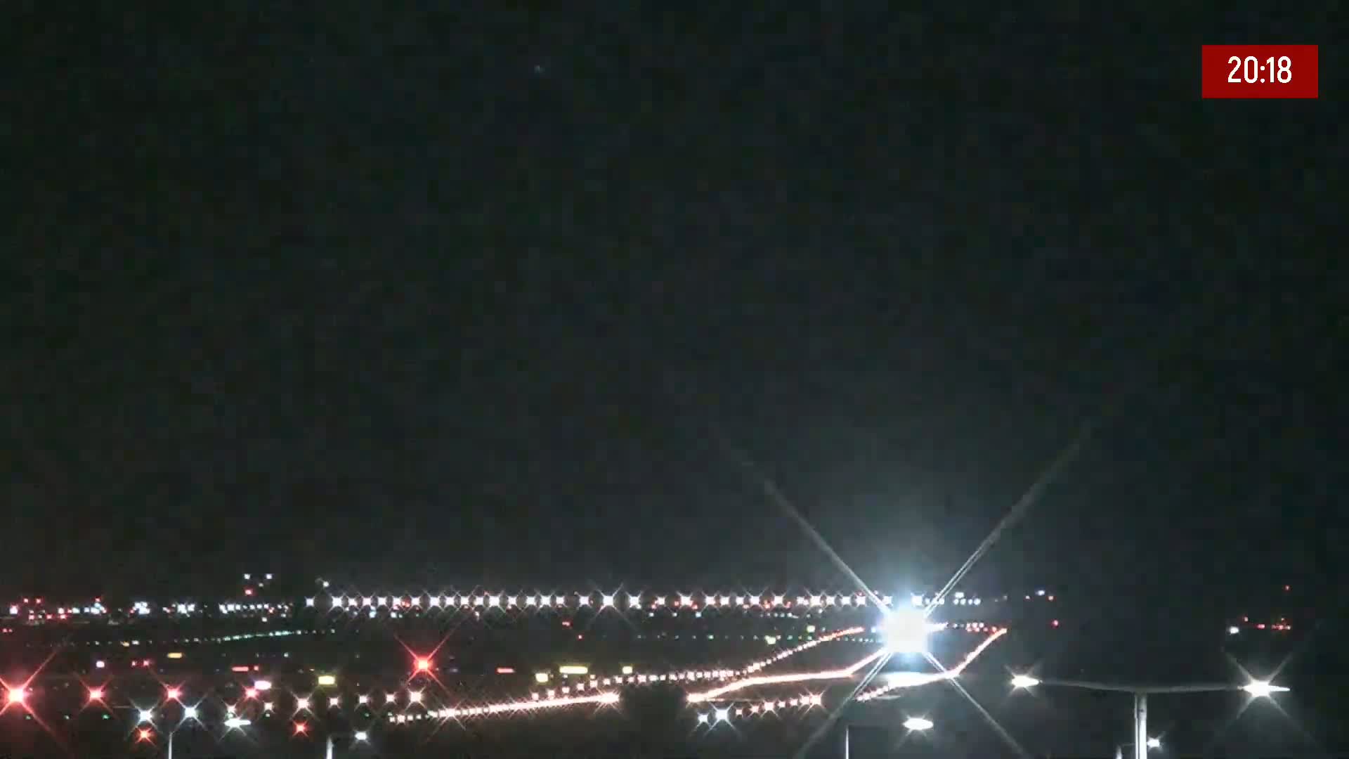 A nighttime view of an airport runway with bright lights illuminating the tarmac and surrounding area under a clear, dark sky.