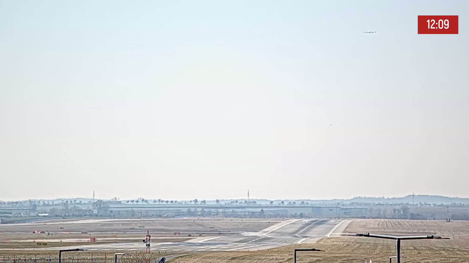 A long shot of an airport runway on a hazy day, with a distant treeline visible in the background.