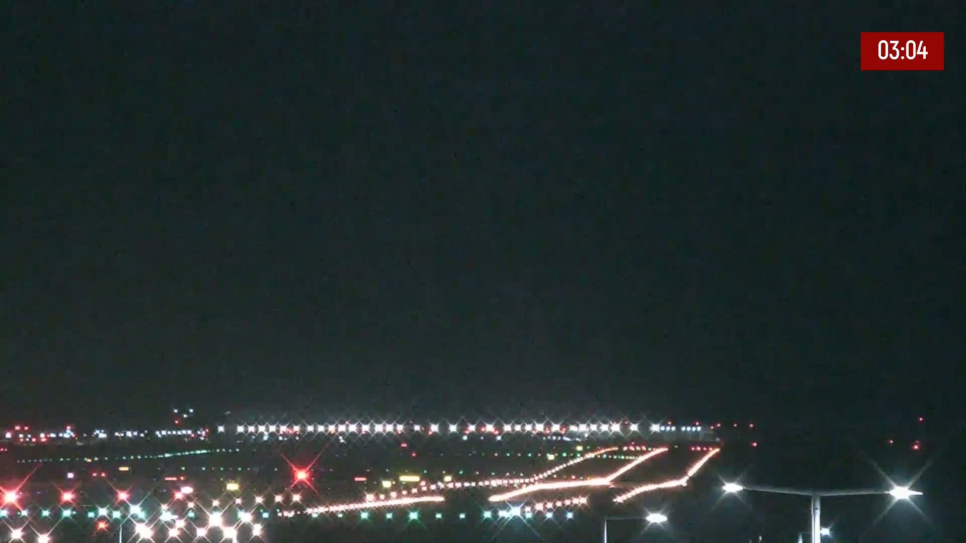 A nighttime view of an airport runway illuminated with lights under a dark sky.