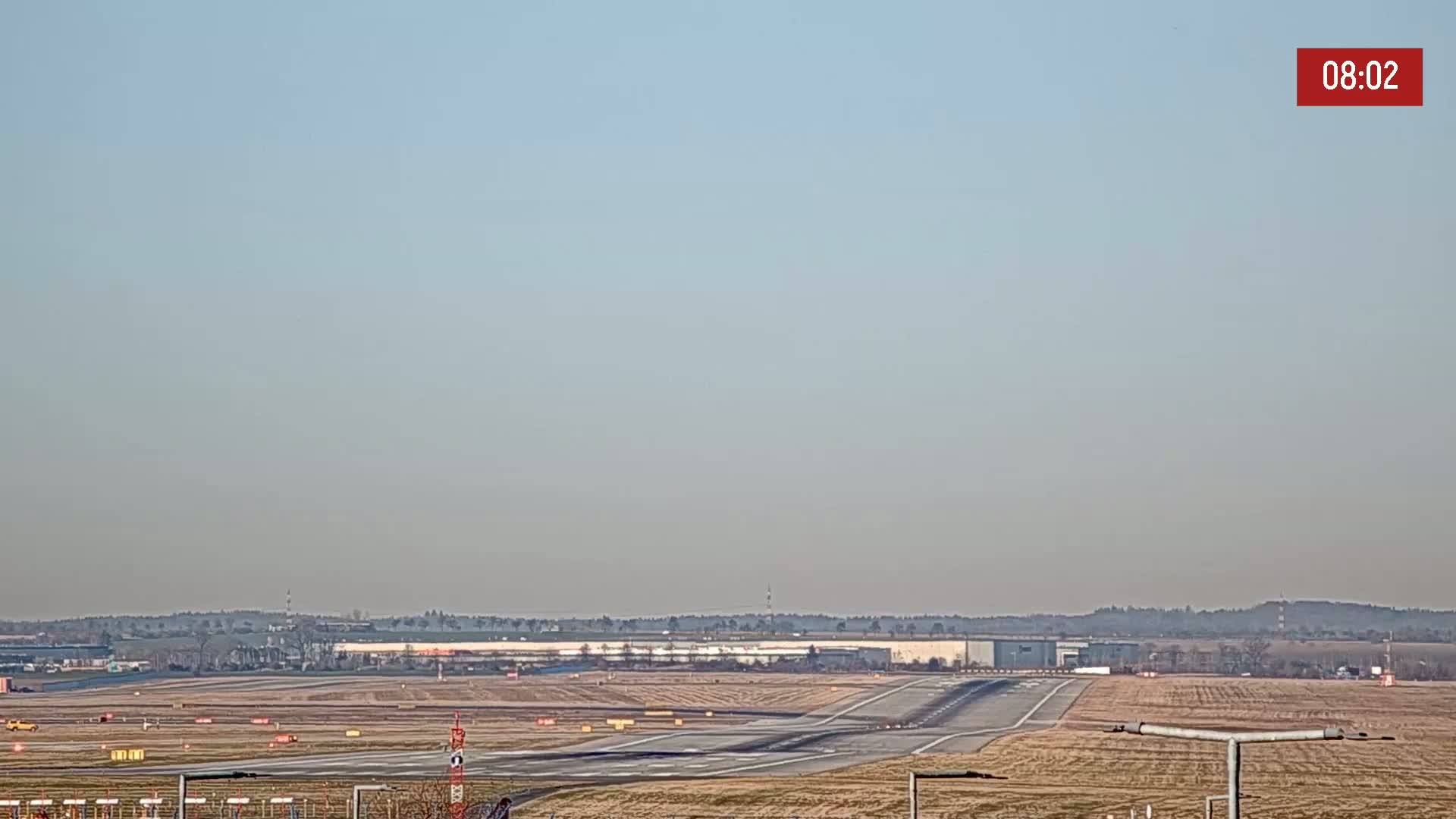 A long runway at an airport is visible under a clear, light-blue sky.
