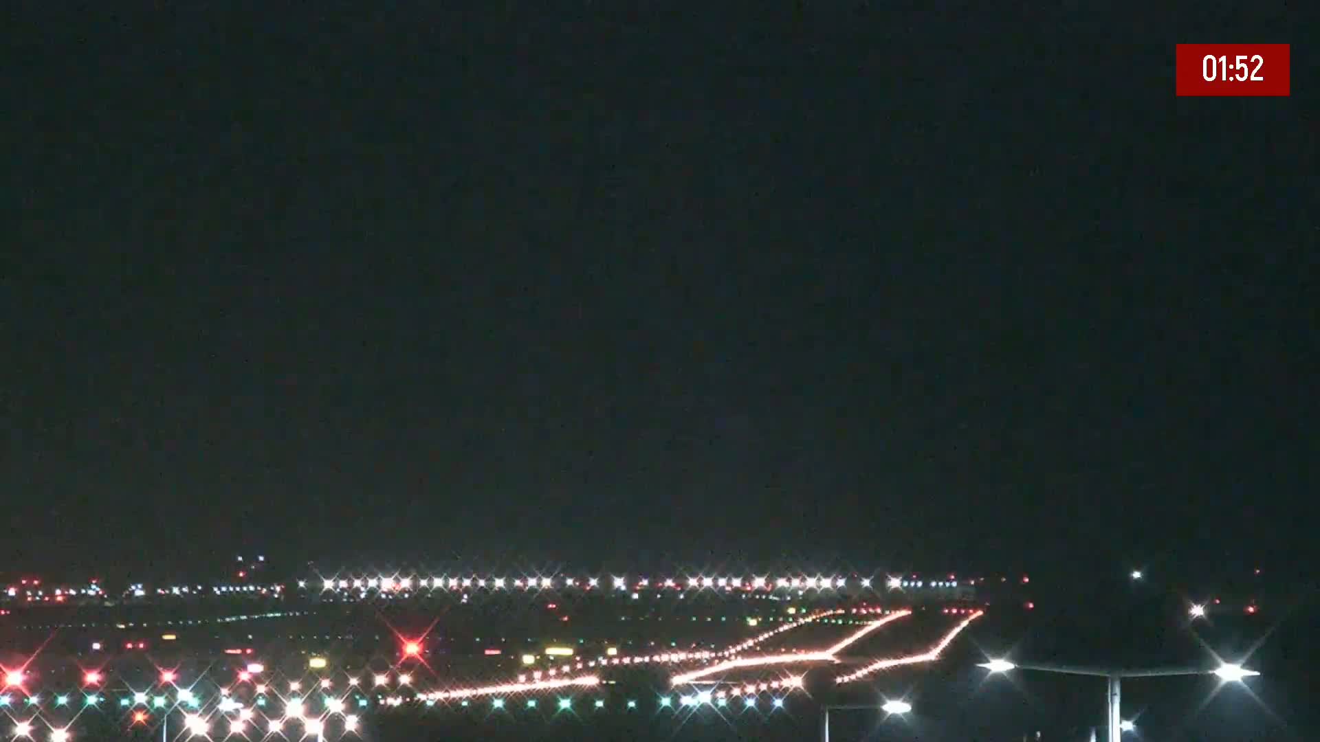 A nighttime view of an airport runway illuminated with lights under a clear, dark sky.