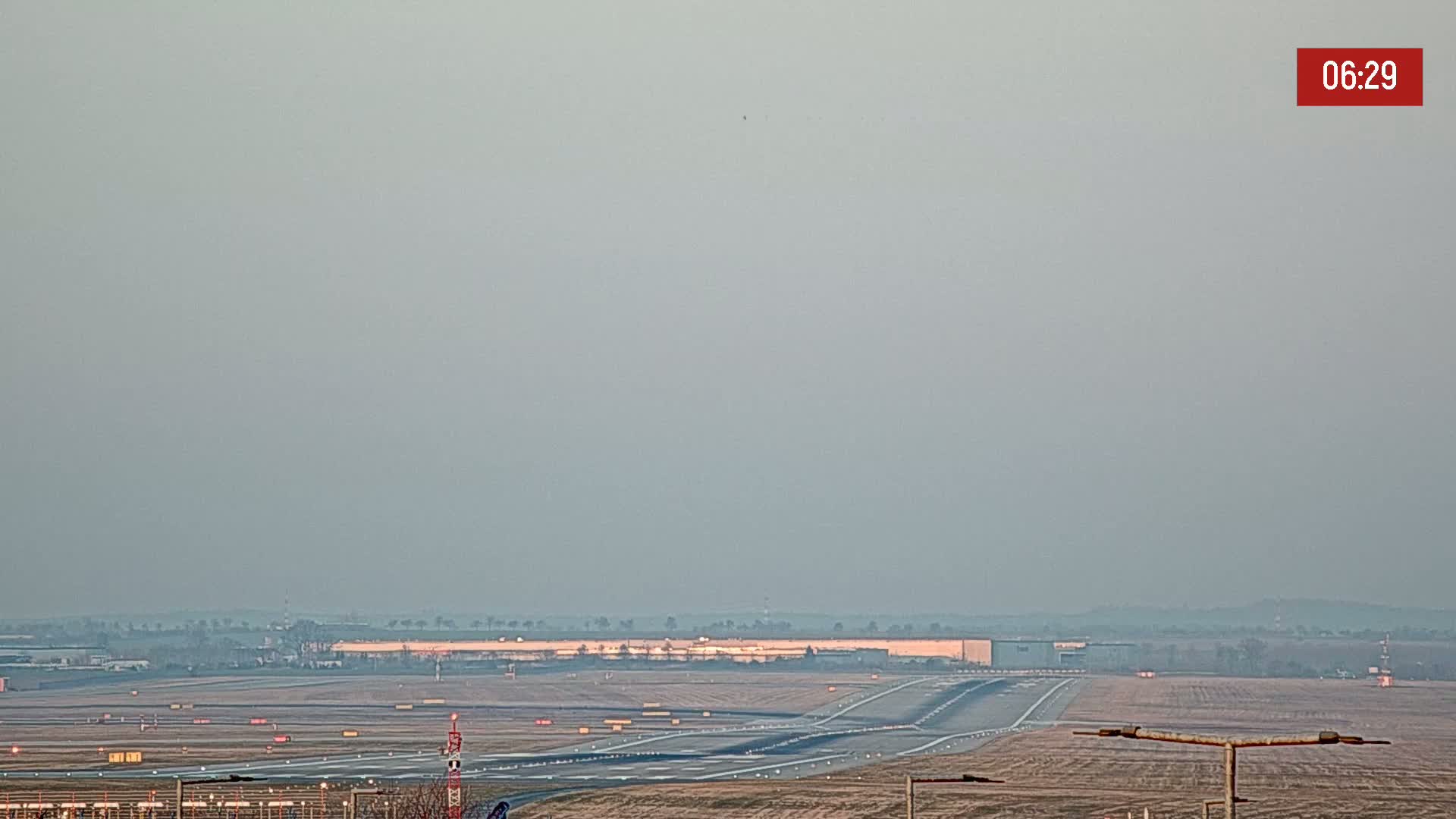 A hazy view of an airport runway and surrounding buildings on a partly cloudy day.