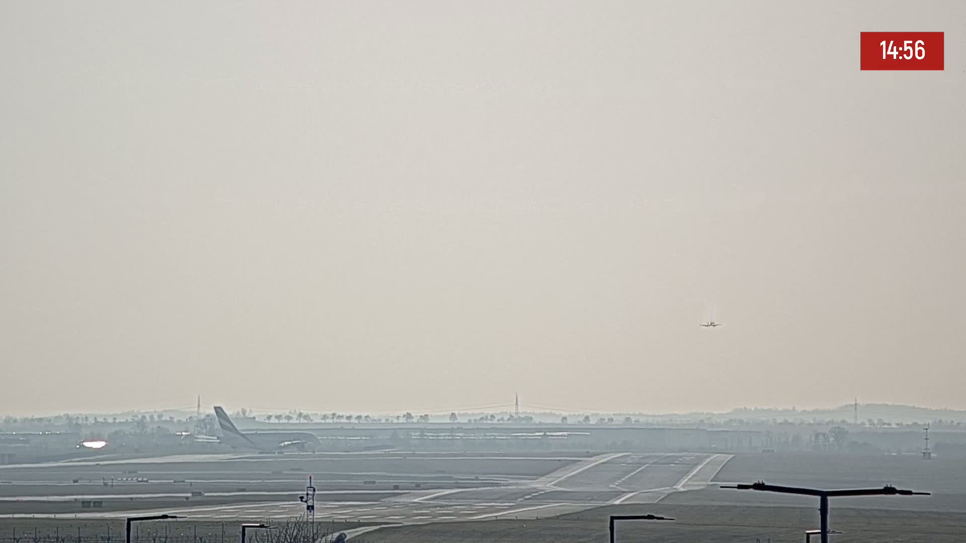 A hazy airport runway with two airplanes, one on the ground and one in the air.