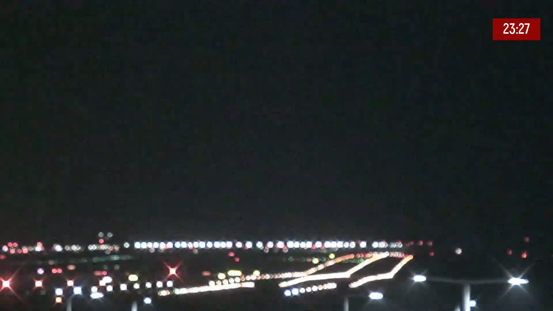 At night, a long runway with lights and moving vehicles is visible under a clear, dark sky.