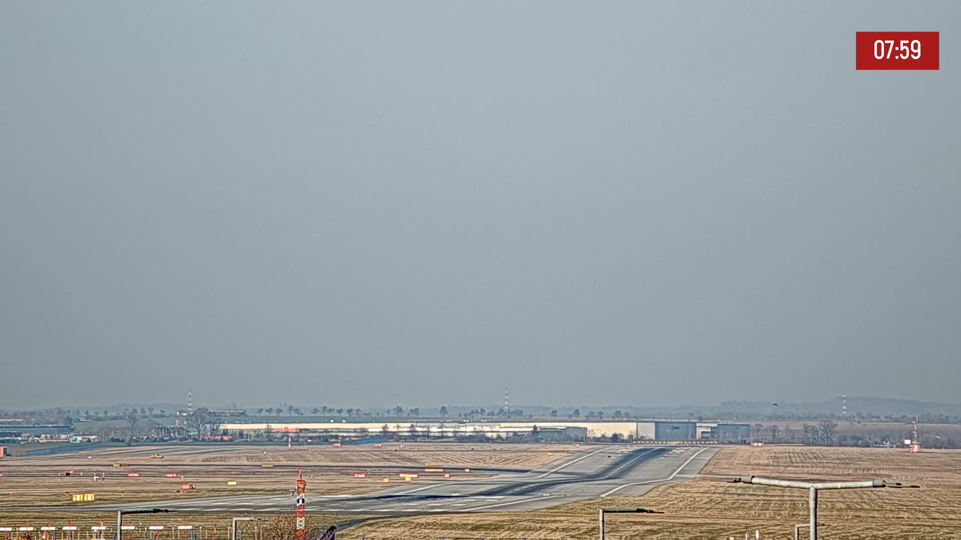 A hazy airport runway and surrounding landscape are visible under a light gray sky.