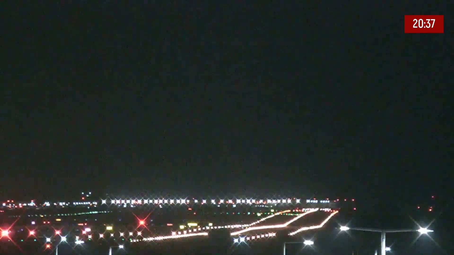 At night, a long runway with bright lights is visible, indicating an airport under dark, clear skies.