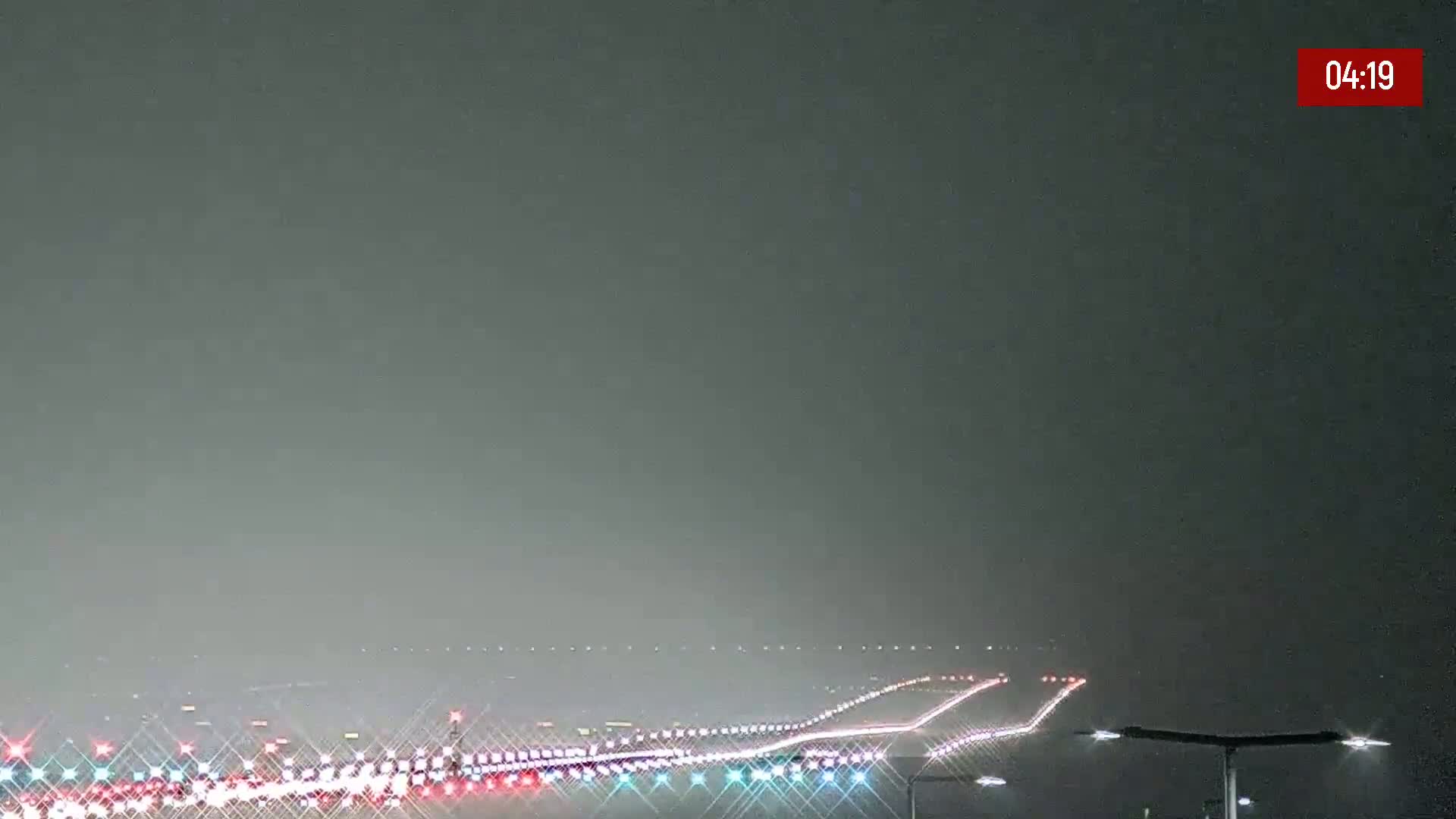 A hazy night scene shows a highway with distant headlights visible under a dark, overcast sky.