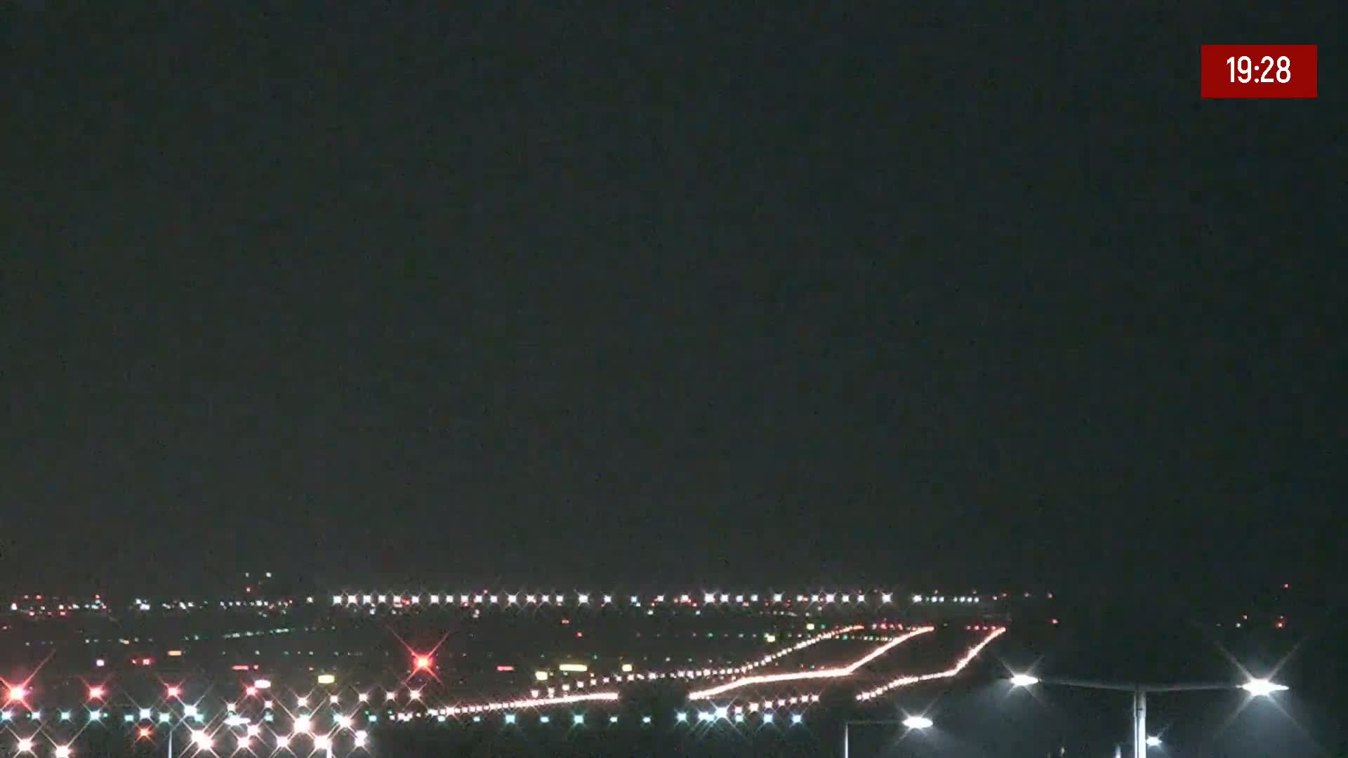 A nighttime long shot of an airport runway illuminated by lights under a dark sky.