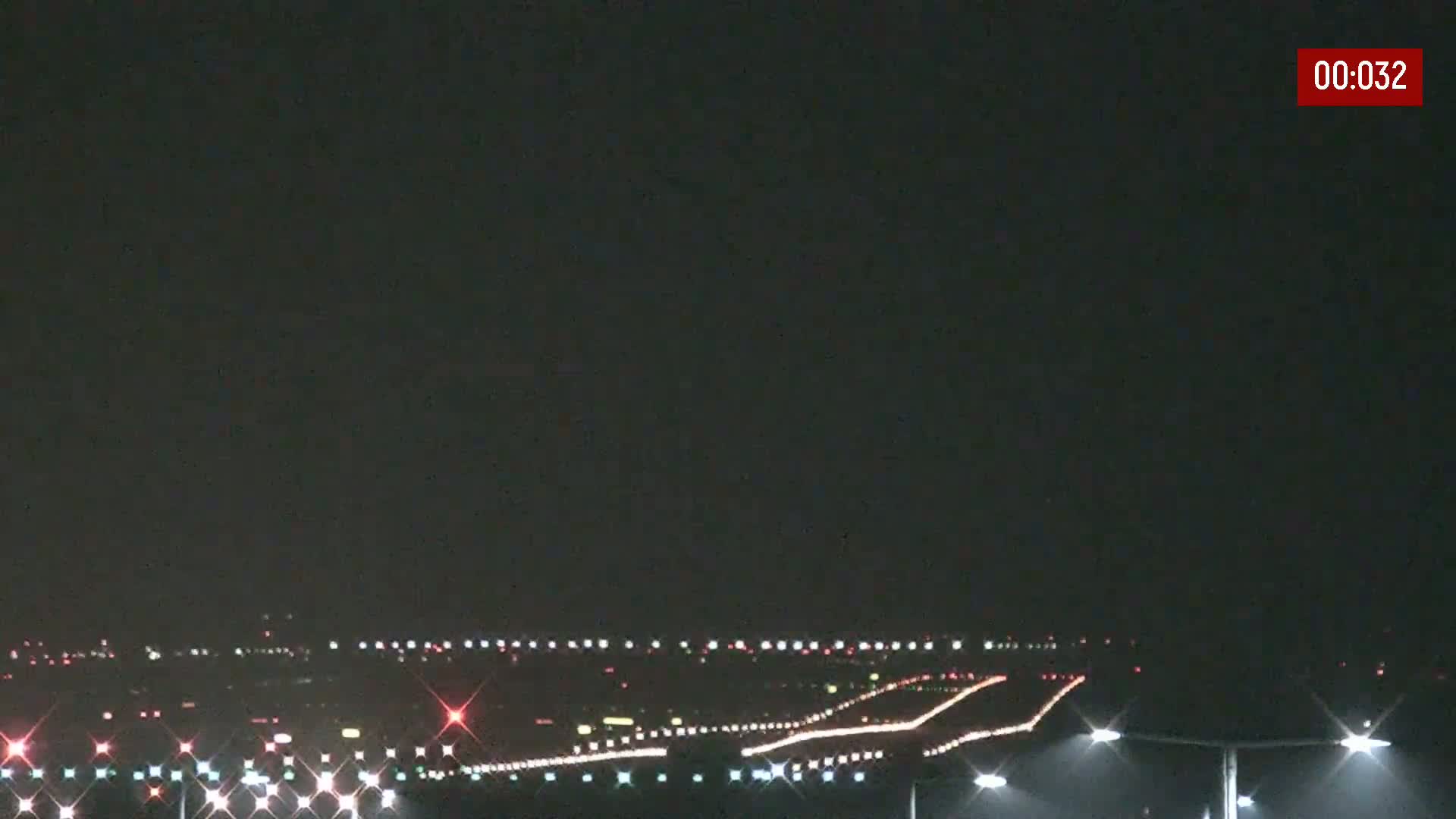 A nighttime long shot of a runway with lights illuminated under a dark sky.