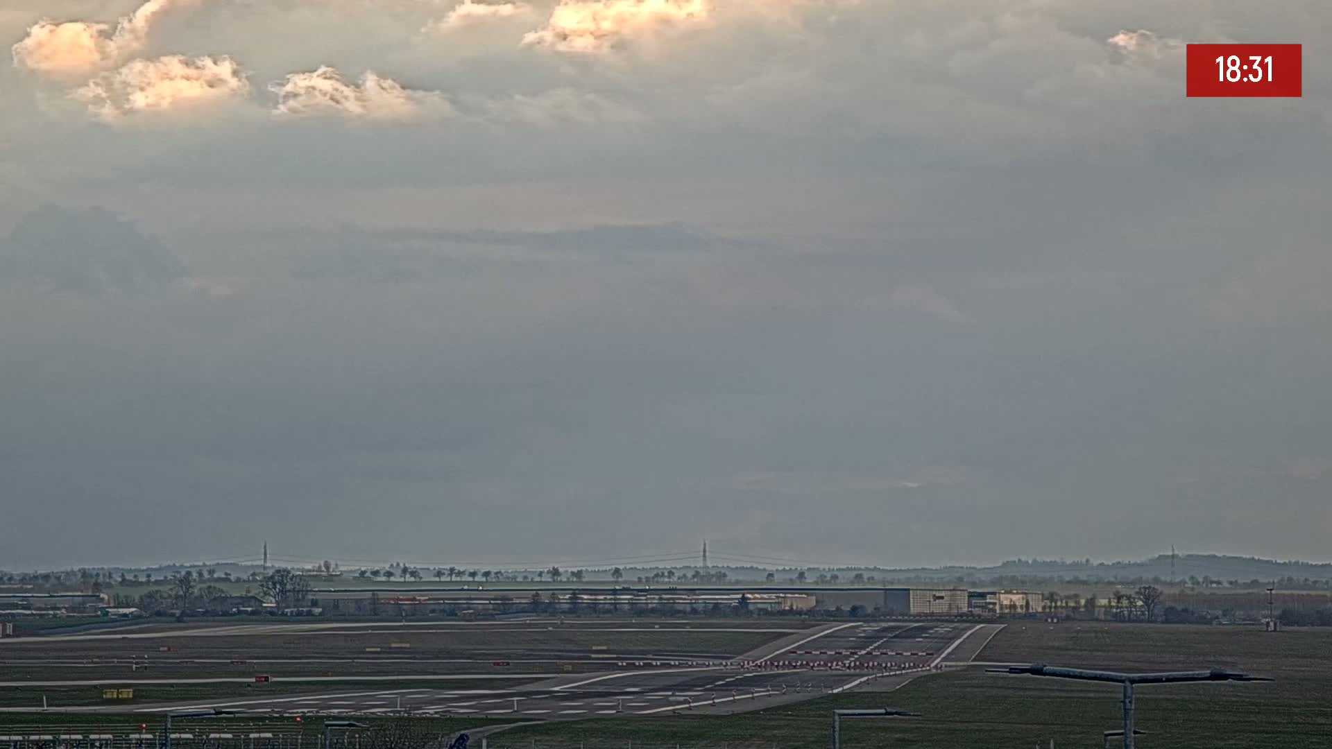 An overcast sky hangs over an airport runway with surrounding buildings and flat land.