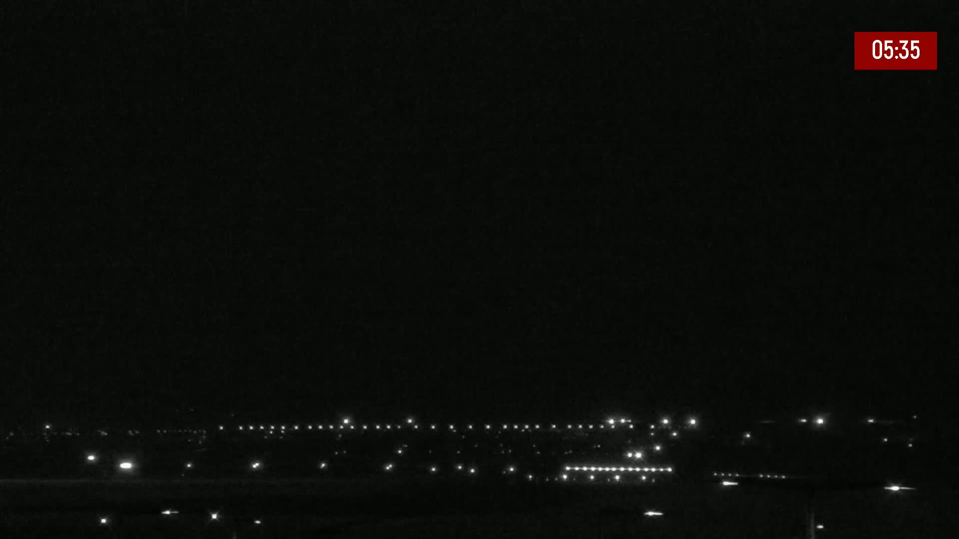 A nighttime, dark scene shows a distant line of lights on the horizon.