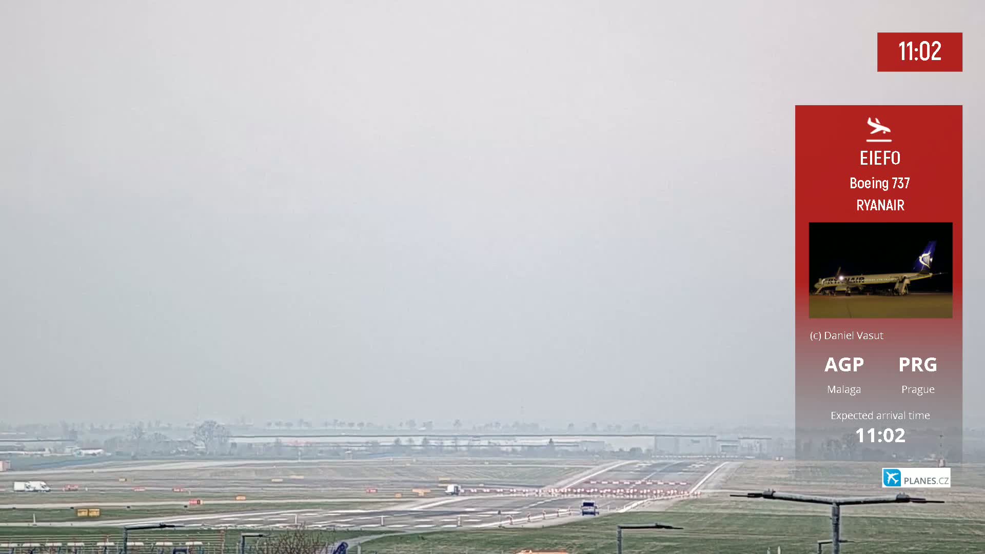 A hazy view of an airport runway with a few vehicles and workers visible in the distance.