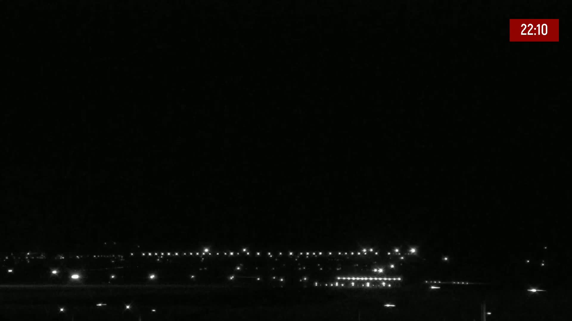 A dark night scene shows a distant line of lights from a town or city under a clear, dark sky.