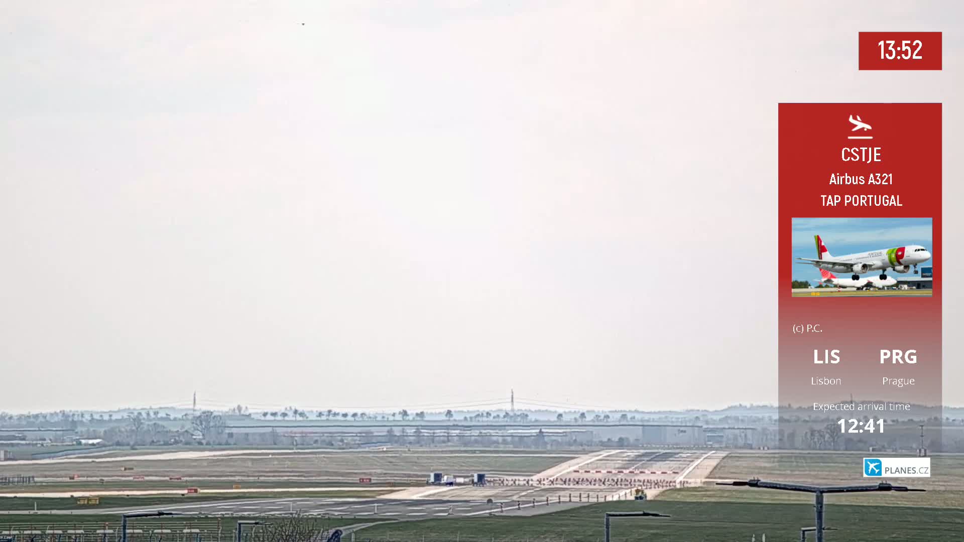 A long shot of an airport runway on an overcast day shows an empty runway with some ground vehicles visible in the distance.