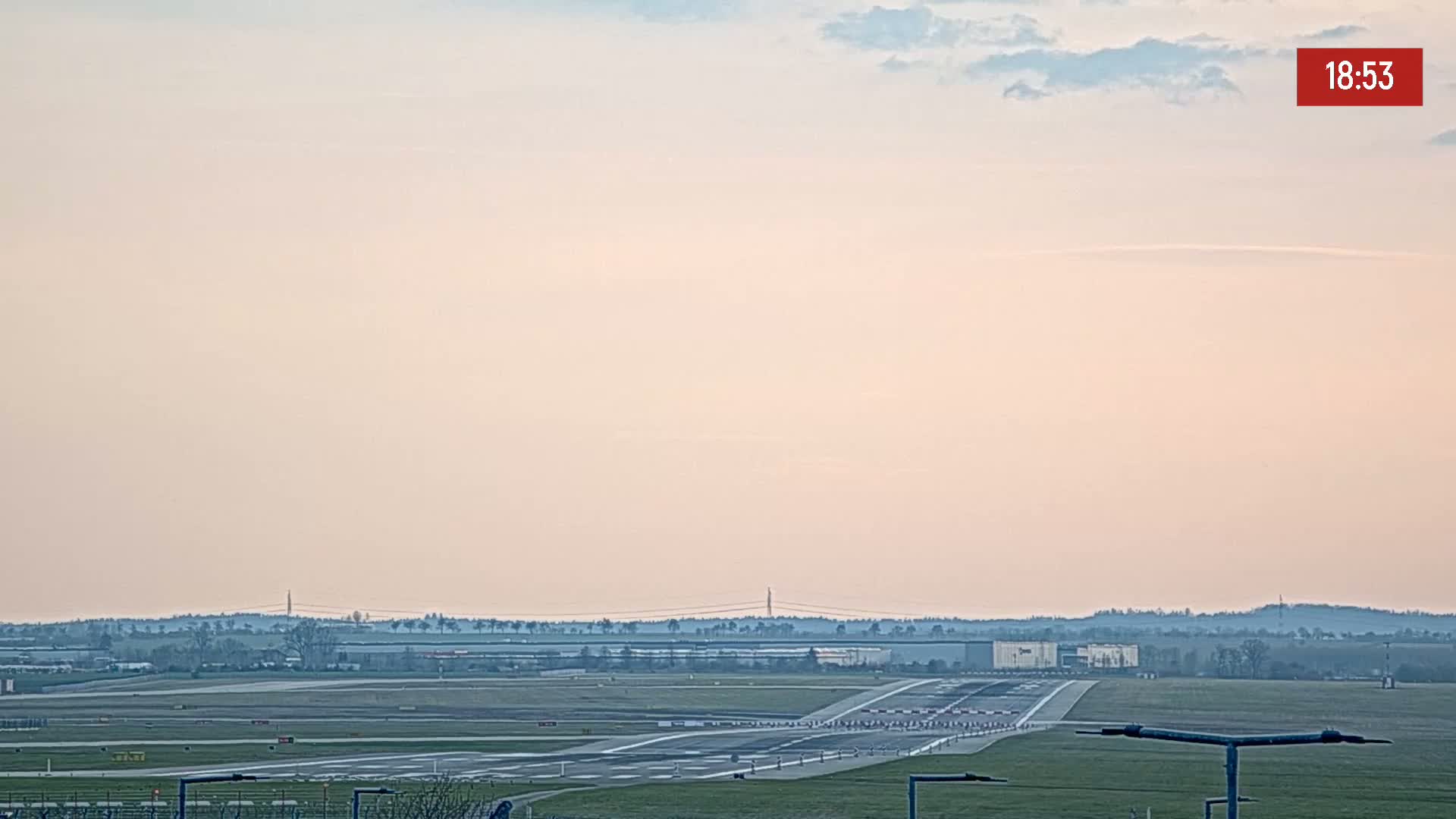 A long runway at an airport stretches towards a hazy horizon under a pale pink and light blue sky.