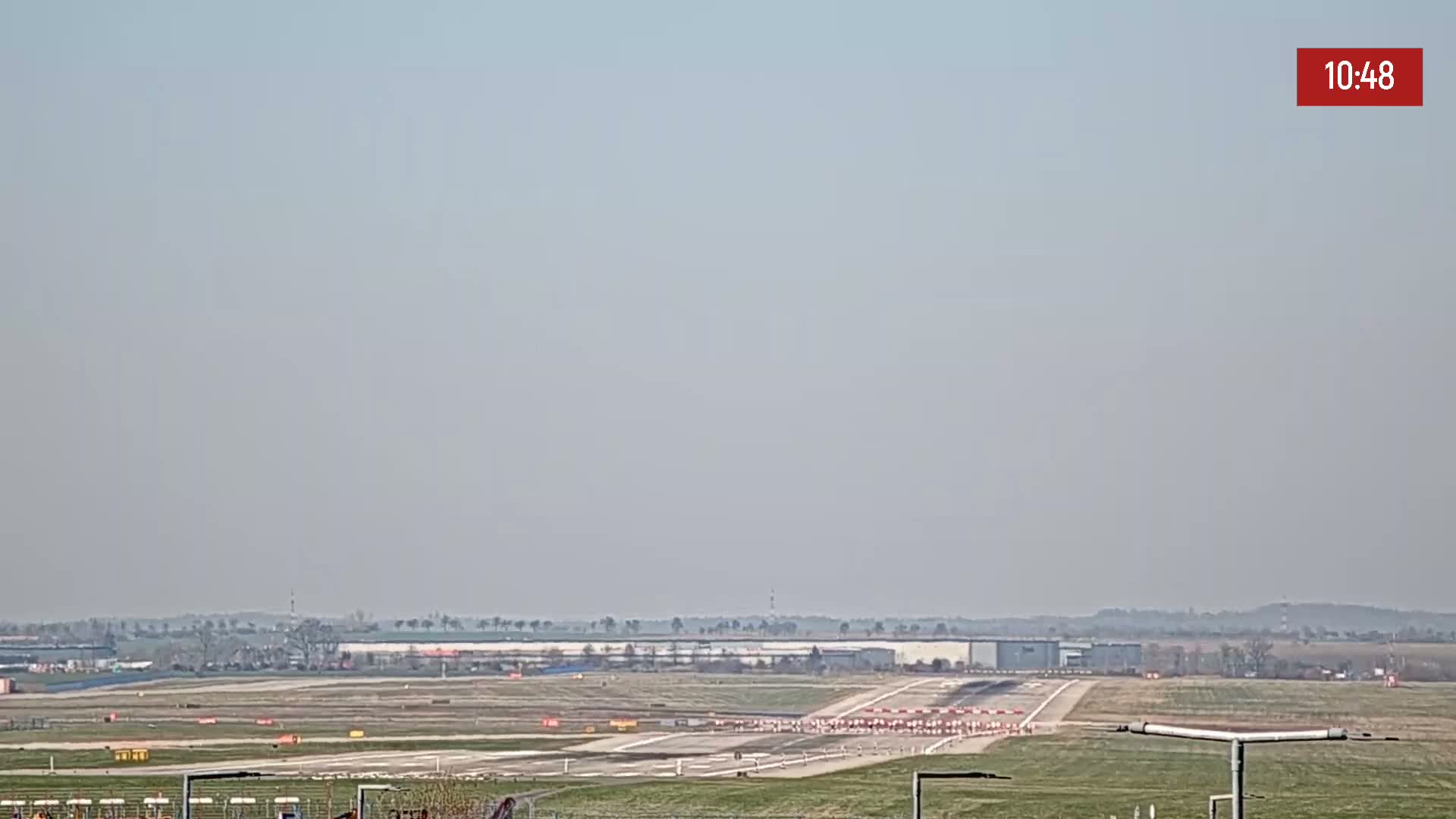 A hazy, long-range view of an airport runway with some construction barriers and equipment visible, under a light-grey sky.