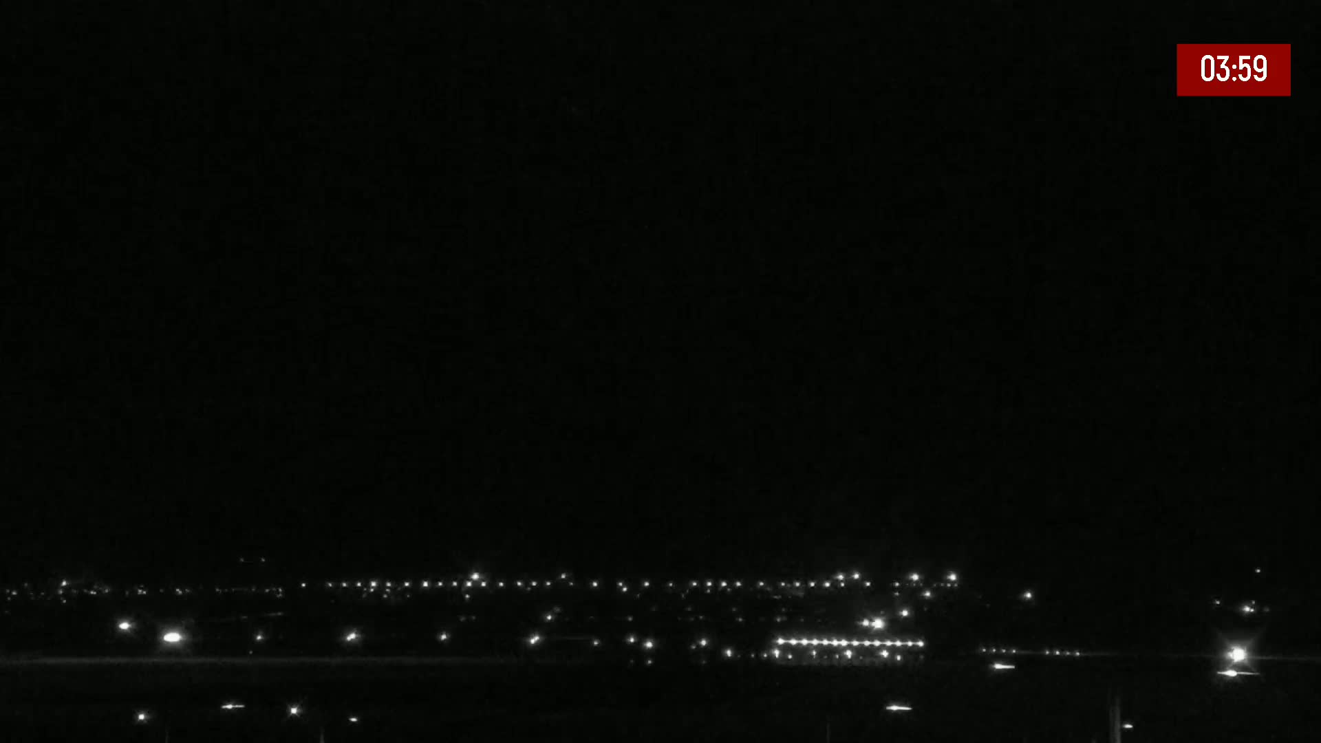 A dark, nighttime view of a distant town's lights spread across a flat landscape.