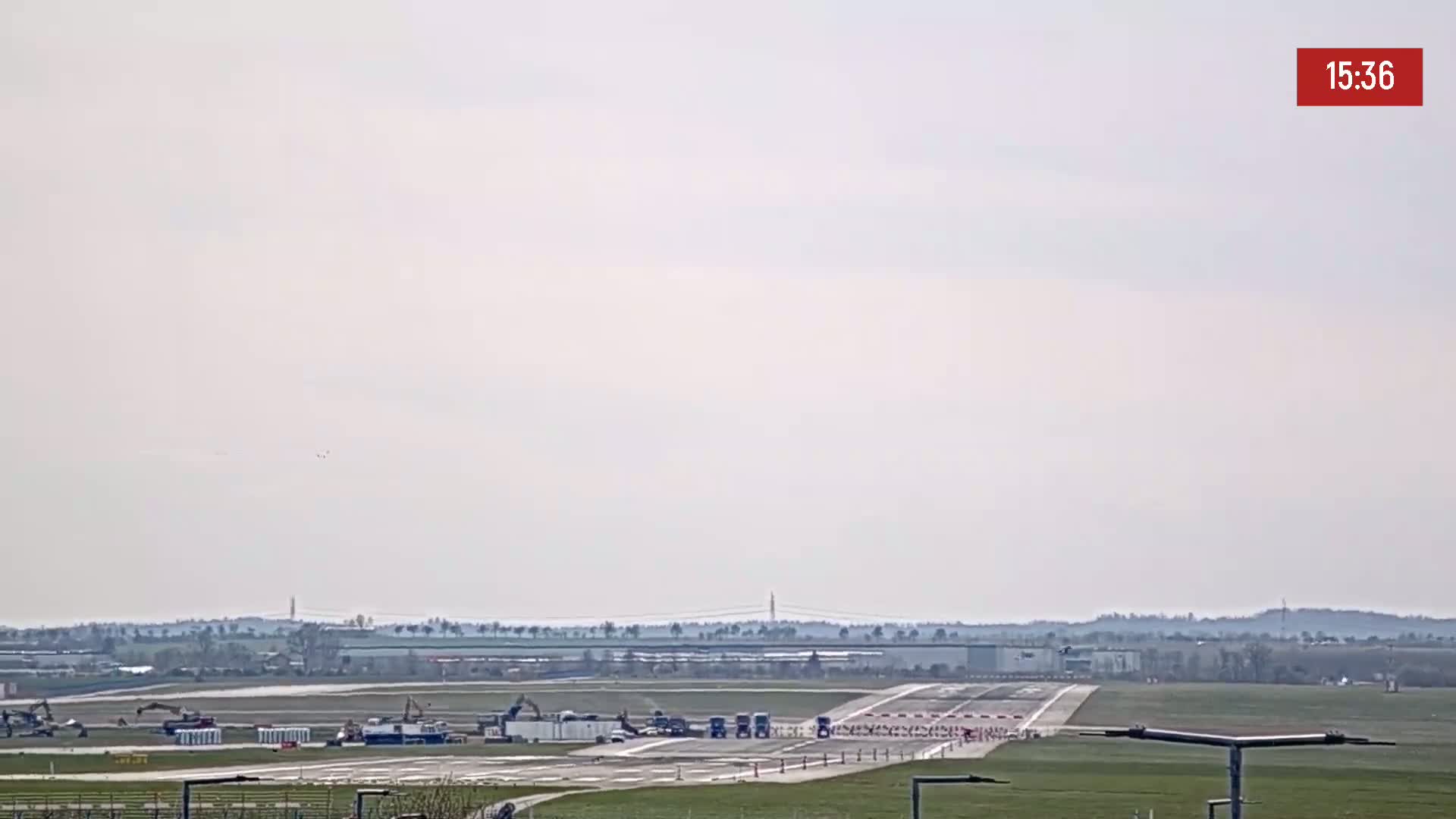 A mostly clear, overcast day at an airport shows construction equipment and vehicles on a runway.
