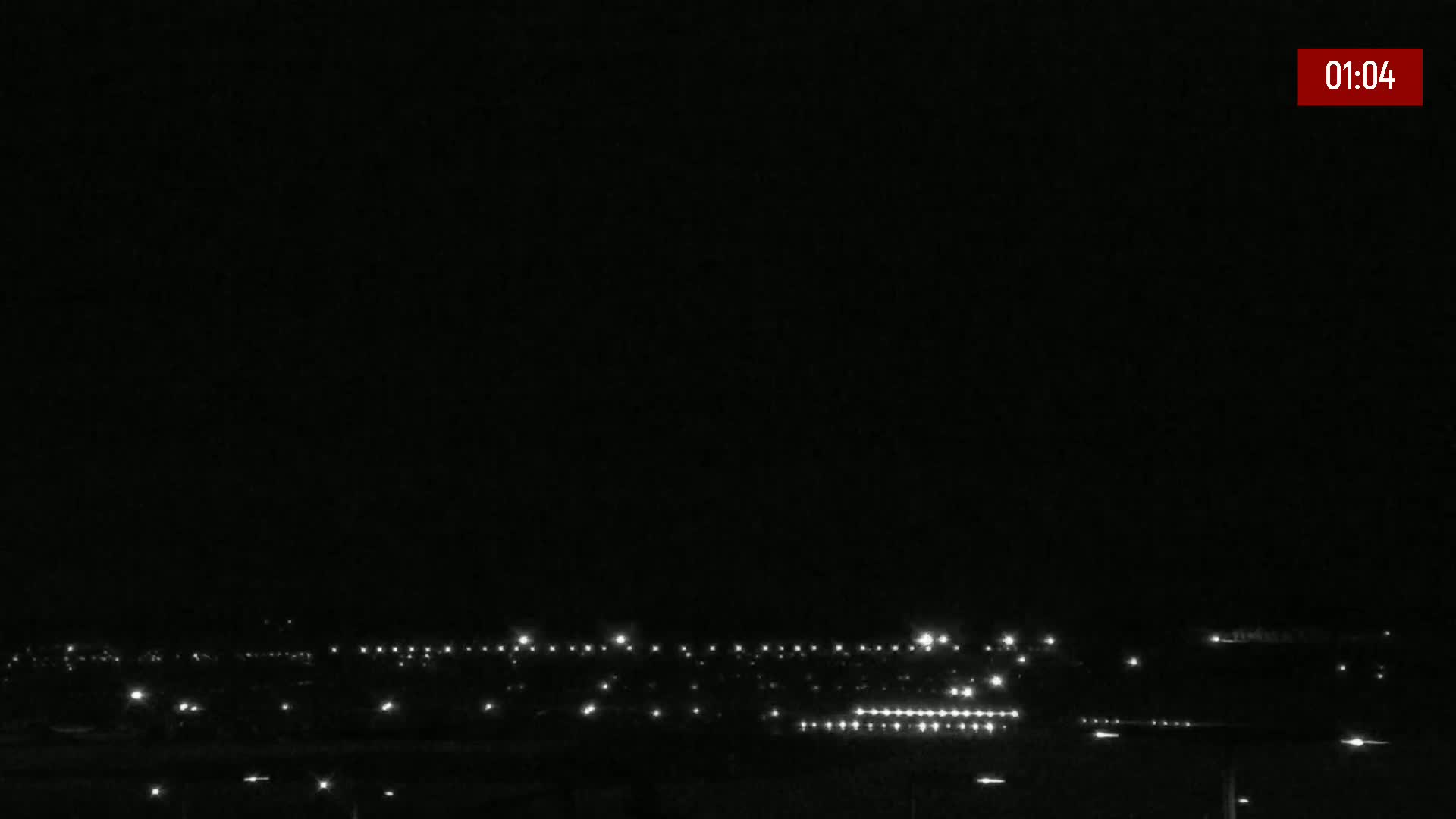 A nighttime, long shot of a distant cityscape illuminated by faint lights under a clear, dark sky.