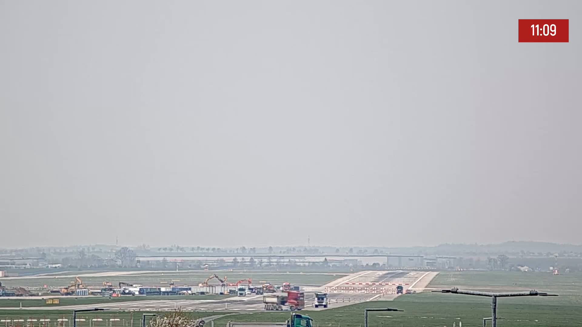 Construction vehicles are visible on a hazy runway at an airport.