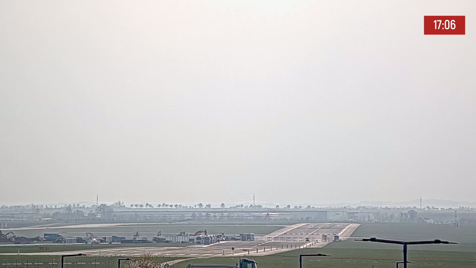 A hazy view of an airport runway with several vehicles and construction equipment present.