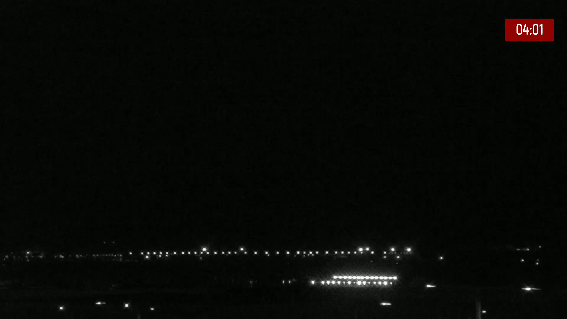 A nighttime long shot shows a line of lights on the ground, possibly runway lights, under a clear, dark sky.