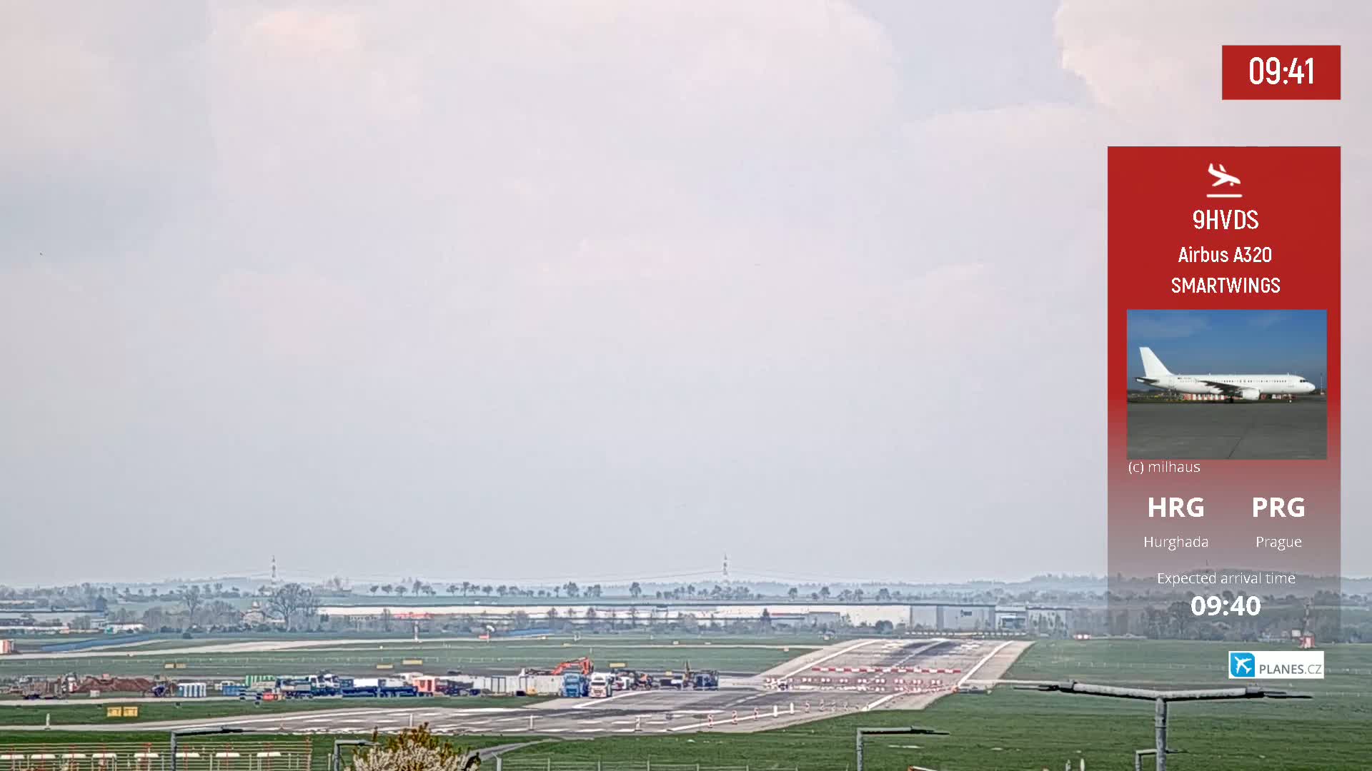 A long-range view of an airport runway on an overcast day shows several ground vehicles near the tarmac.