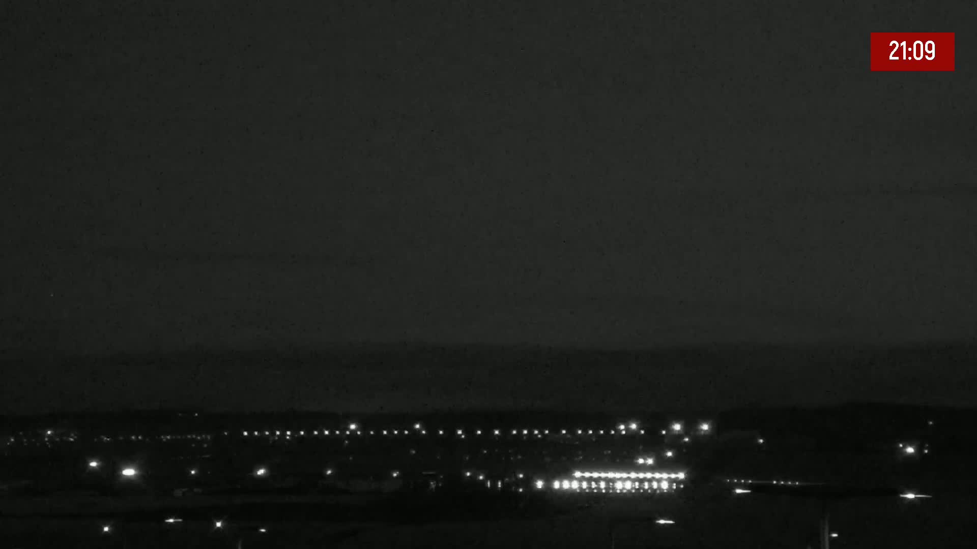 A nighttime long shot of a dimly lit town or city under a dark sky.