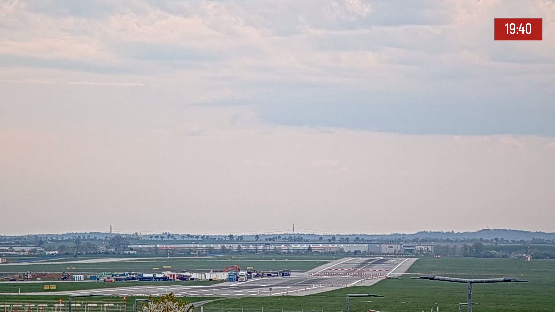 An airport runway is visible under a partly cloudy sky.