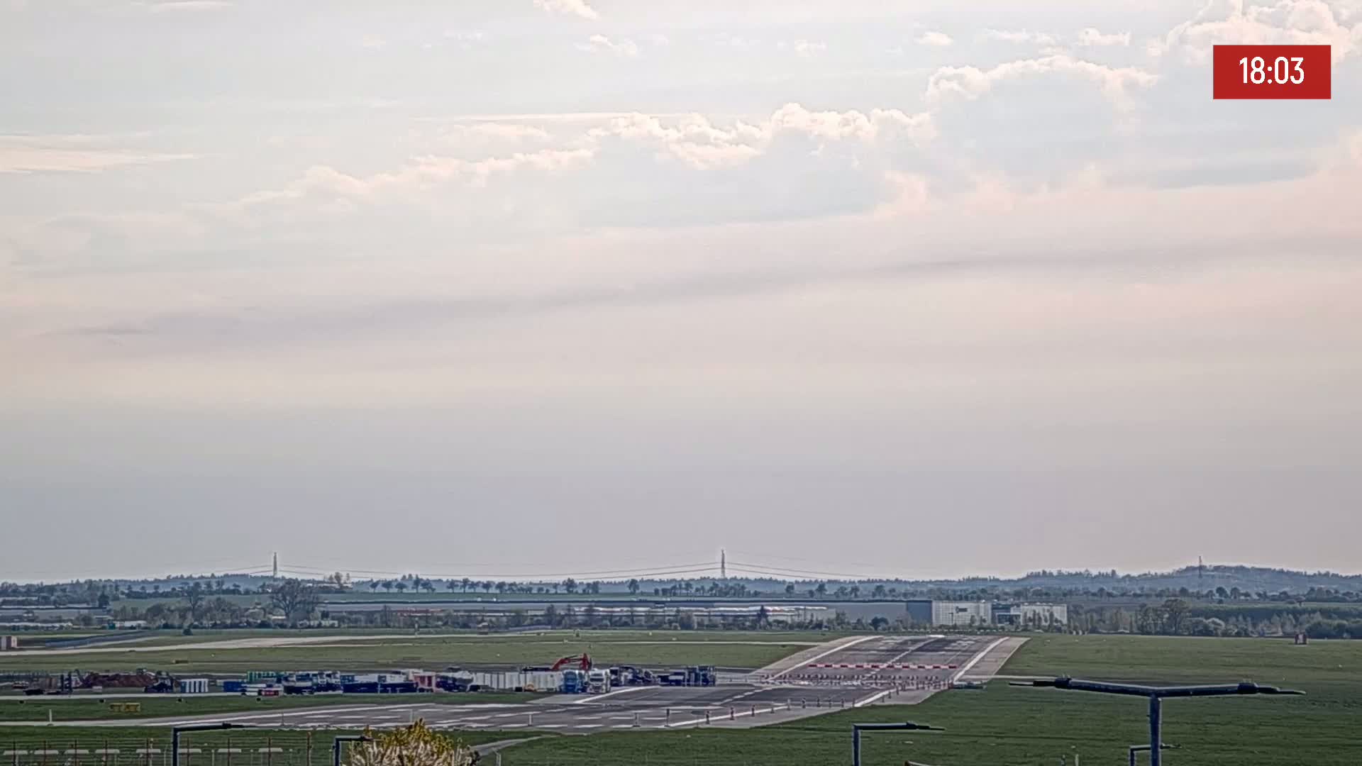A runway with several vehicles parked on it is visible under a partly cloudy sky.