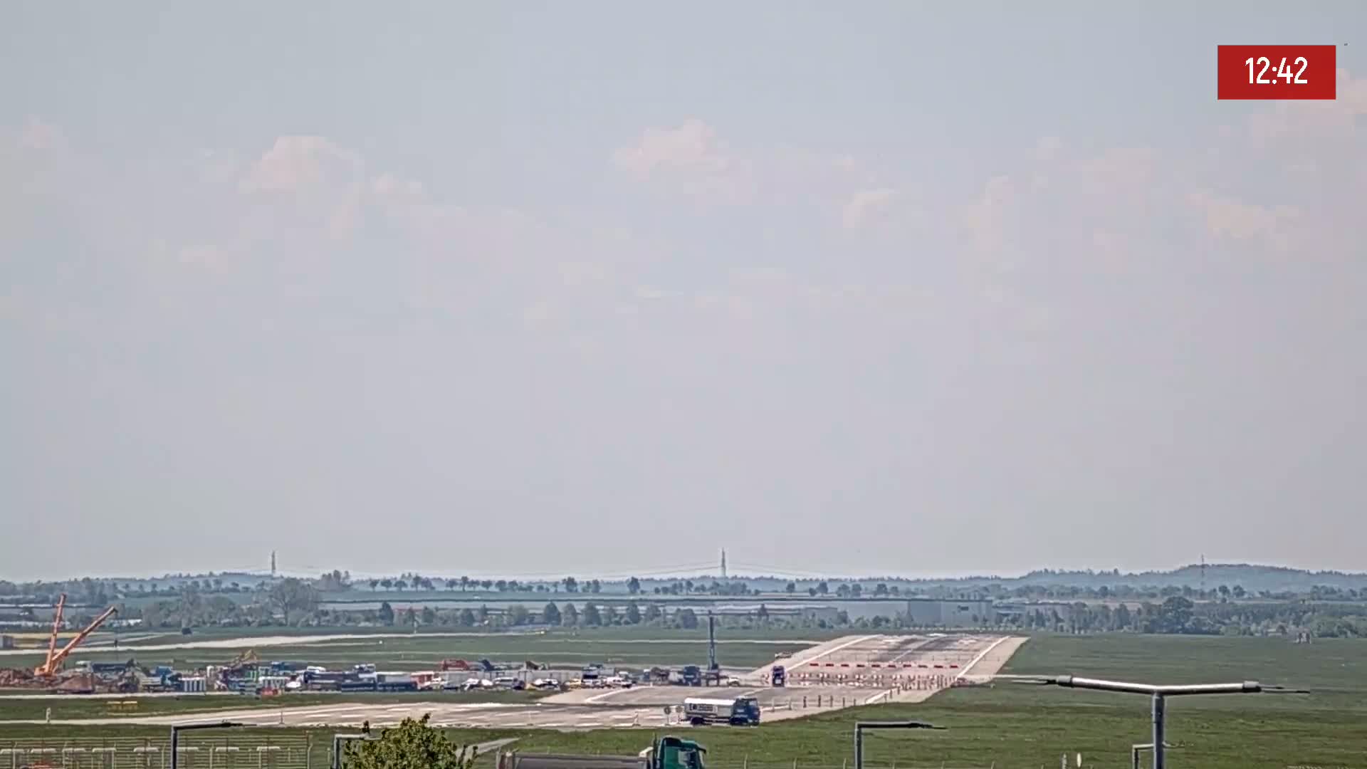 Under a partly cloudy sky, an airport runway is visible with construction equipment and vehicles present on the tarmac.