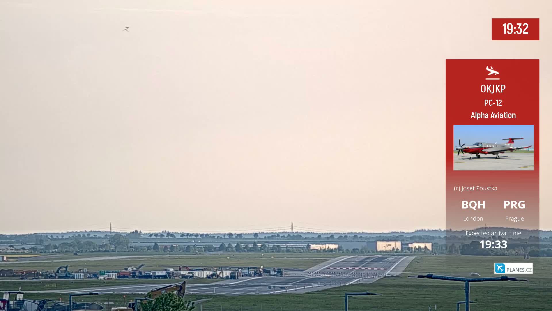 A long shot of an airport runway on a hazy day shows construction equipment and a plane approaching.