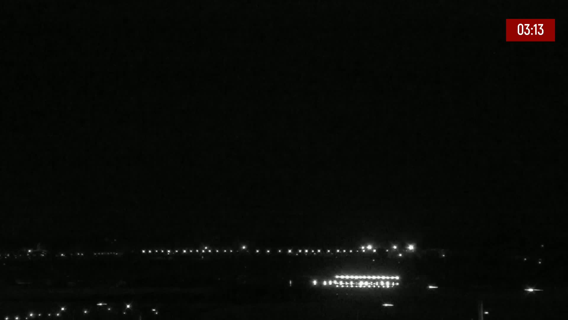 A nighttime, long shot of a dark landscape with a line of lights in the distance under a clear, dark sky.