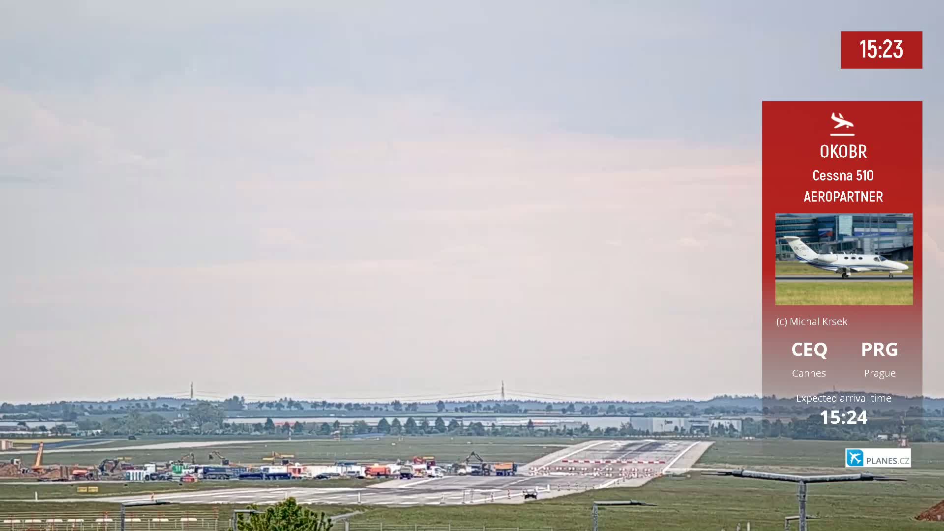 A private jet is expected to arrive at an airport runway under partly cloudy skies, with construction equipment visible on the tarmac.