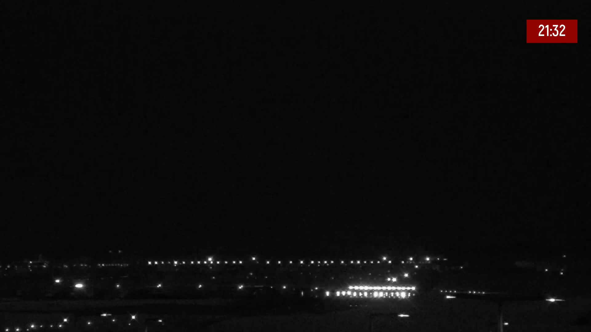 At night, a line of distant lights illuminates a dark landscape under a clear, black sky.