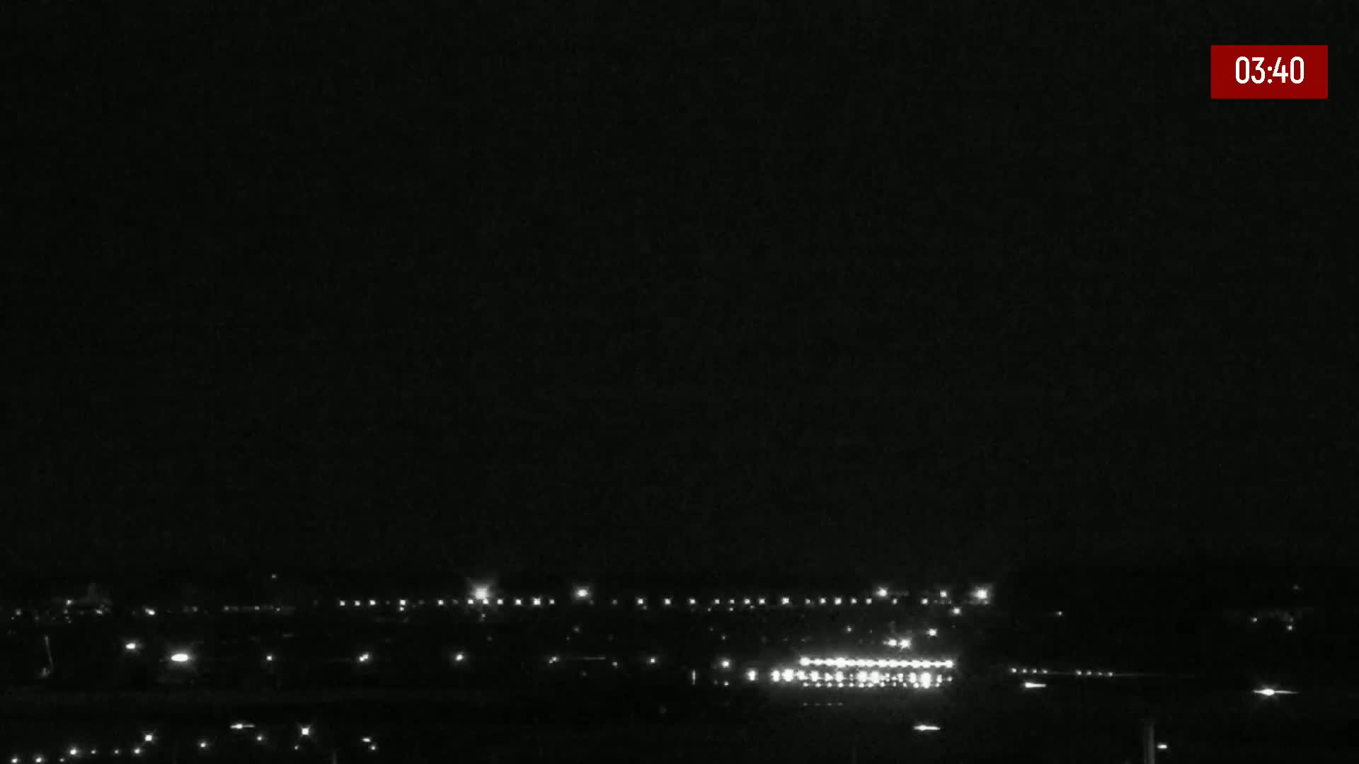 A nighttime long shot shows a line of distant lights, possibly a road or runway, under a dark, clear sky.