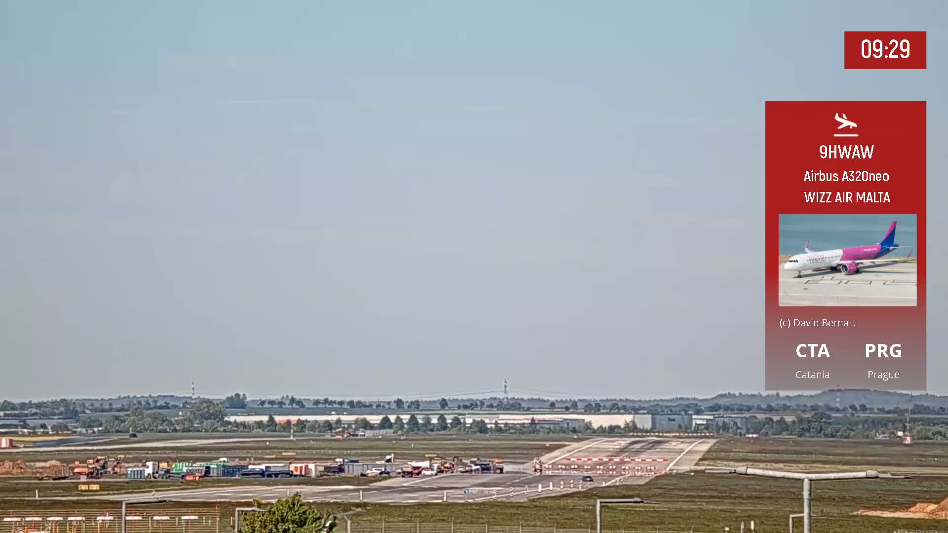 A long view of an airport runway on a hazy day shows construction equipment and vehicles on the tarmac.