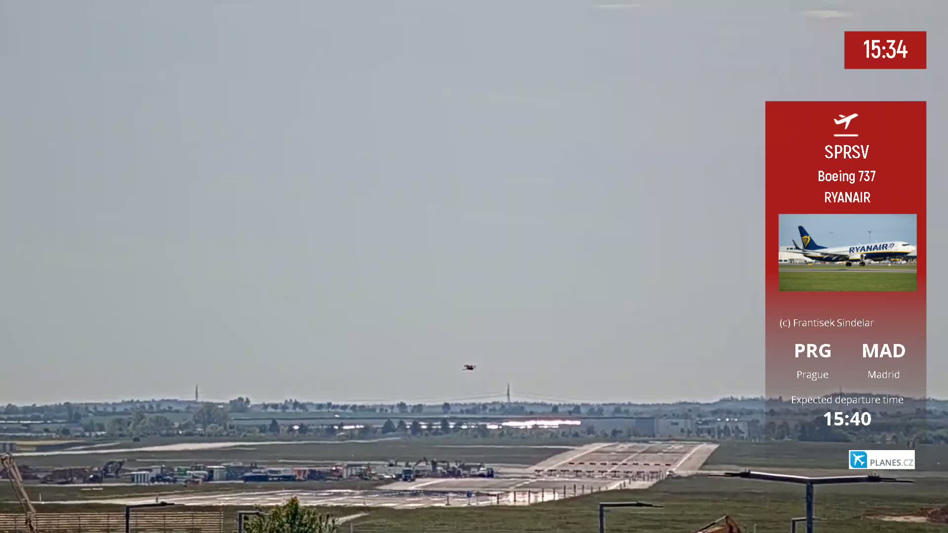 A long shot of an airport runway under a hazy sky, with a small plane in the distance and construction equipment visible.