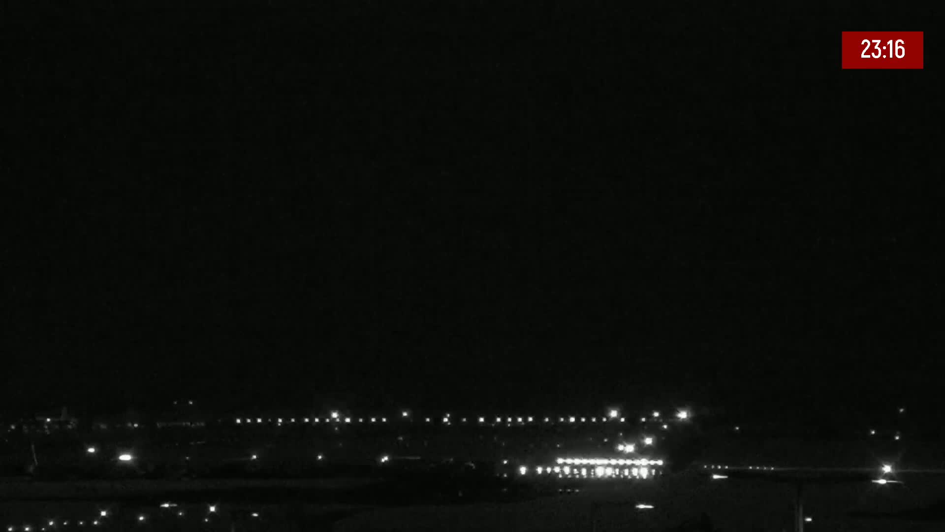 A nighttime, outdoor view shows a line of distant lights, possibly from buildings or vehicles, under a dark, clear sky.