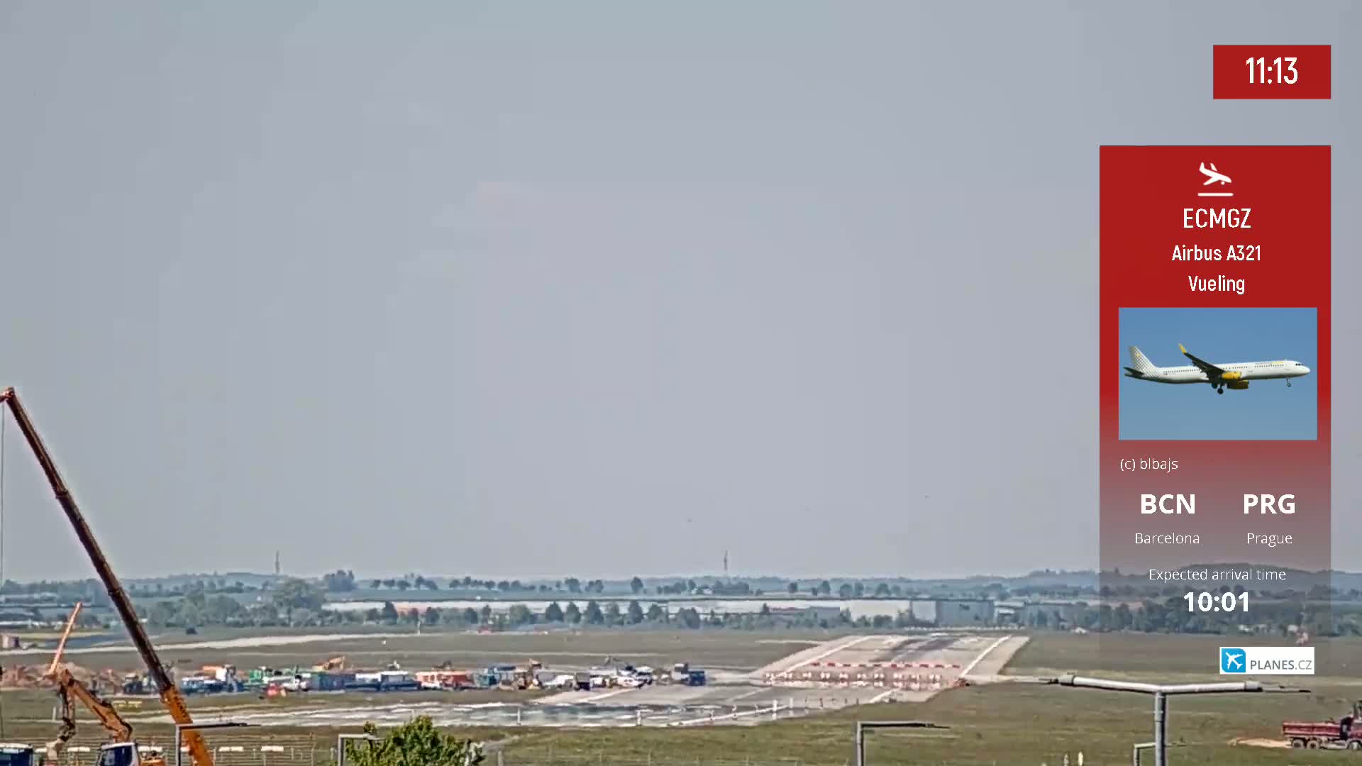 A plane is seen approaching an airport runway under a hazy sky, with construction equipment visible on the tarmac.