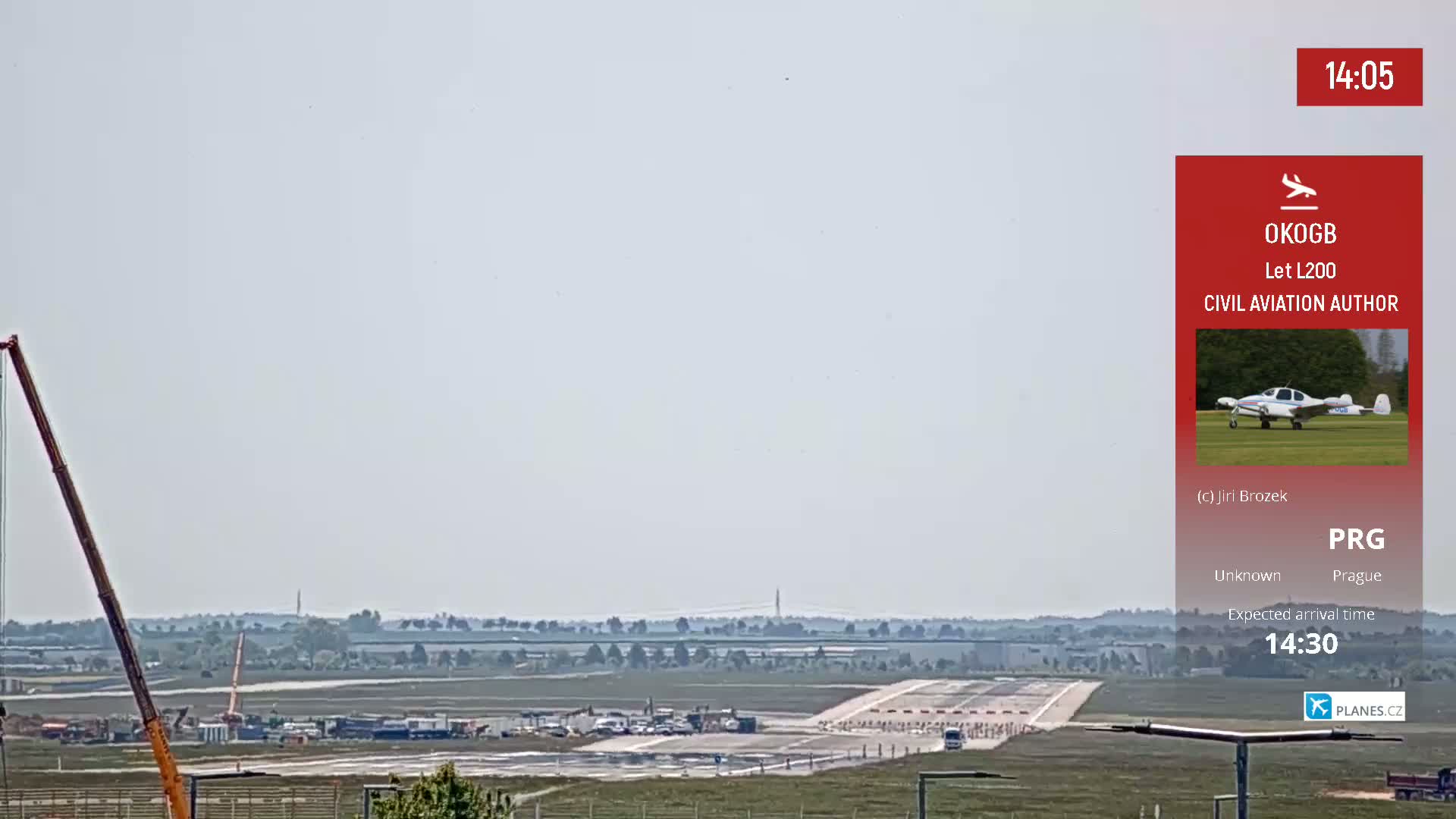 A long crane and construction vehicles are visible on an airport runway under a hazy sky.