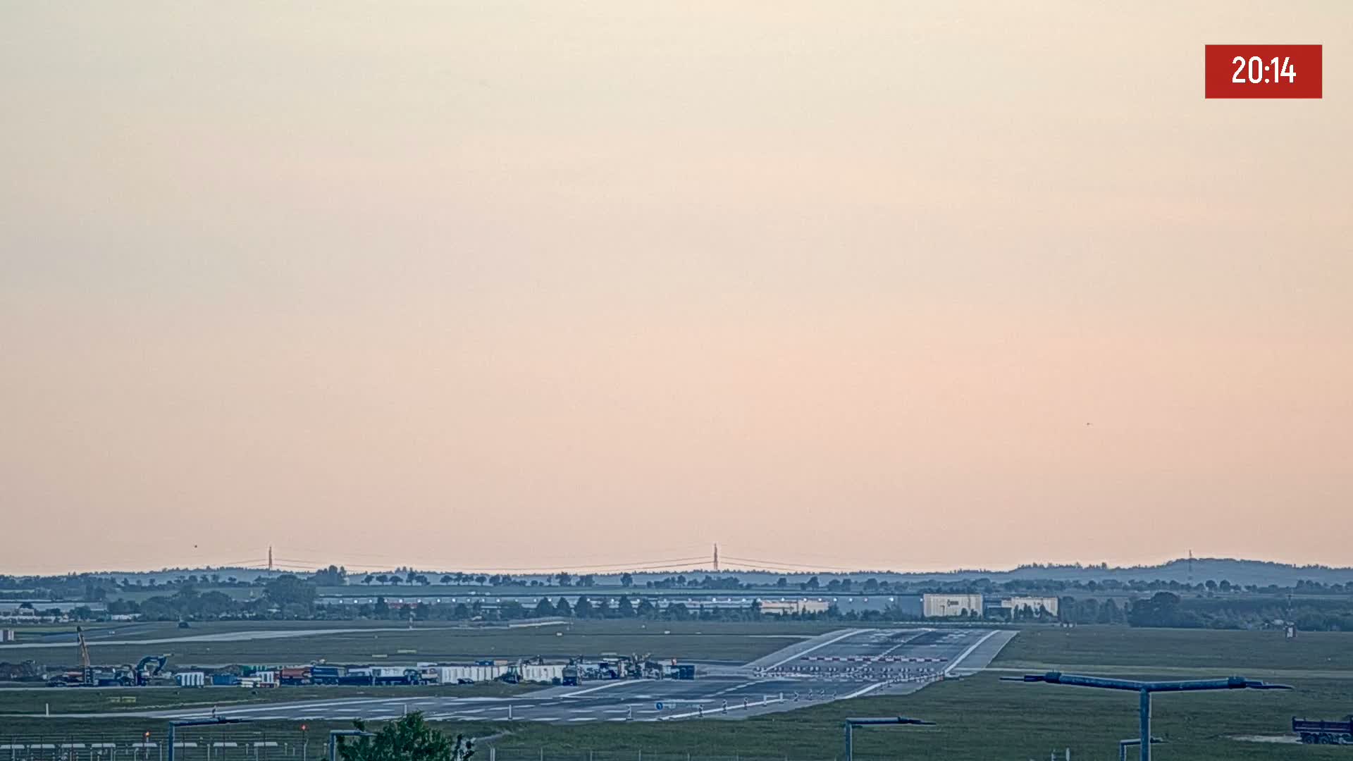 A runway at an airport is visible under a pale pink sunset sky.
