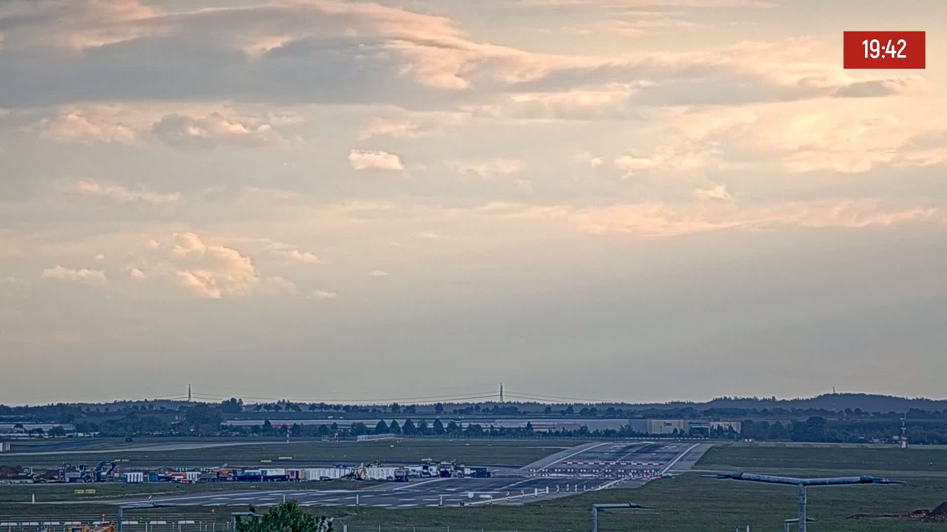 Under a partly cloudy sky, an airport runway is visible with various ground support equipment and vehicles positioned on the tarmac.