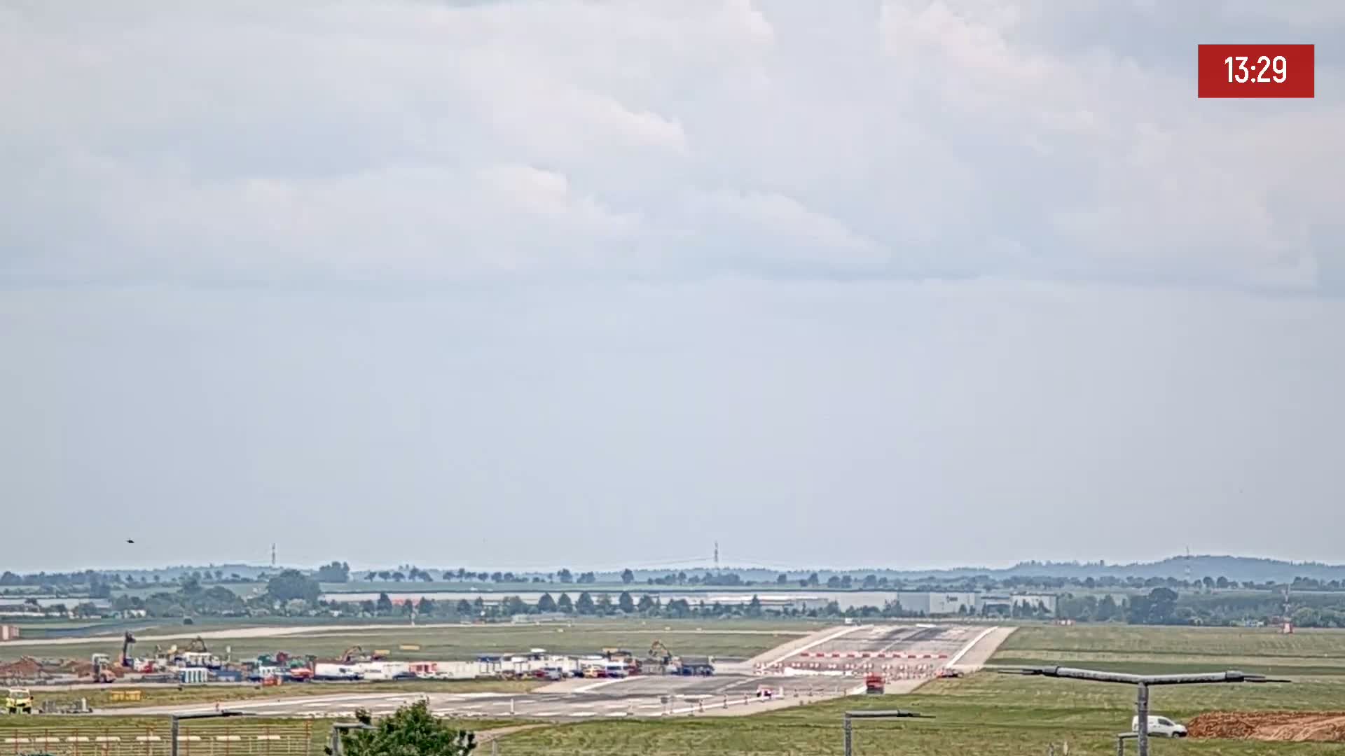 A long runway at an airport with construction equipment and vehicles is visible under a partly cloudy sky.