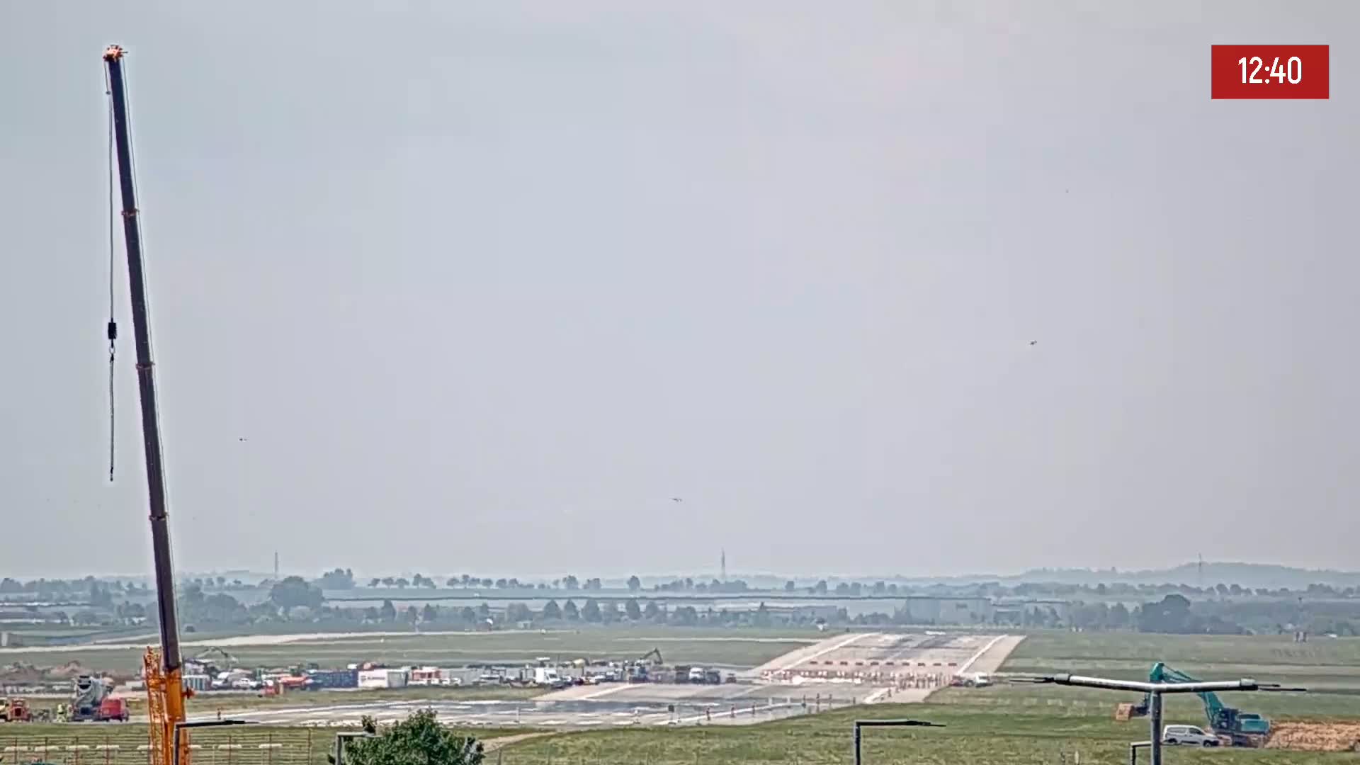 A hazy day shows an airport runway under construction with several pieces of heavy machinery present.