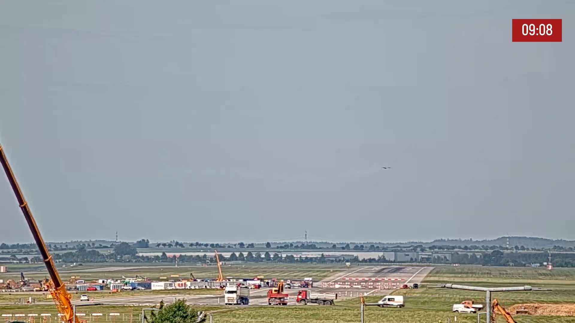 A long runway at an airport under construction on a hazy day, with several pieces of heavy machinery present.