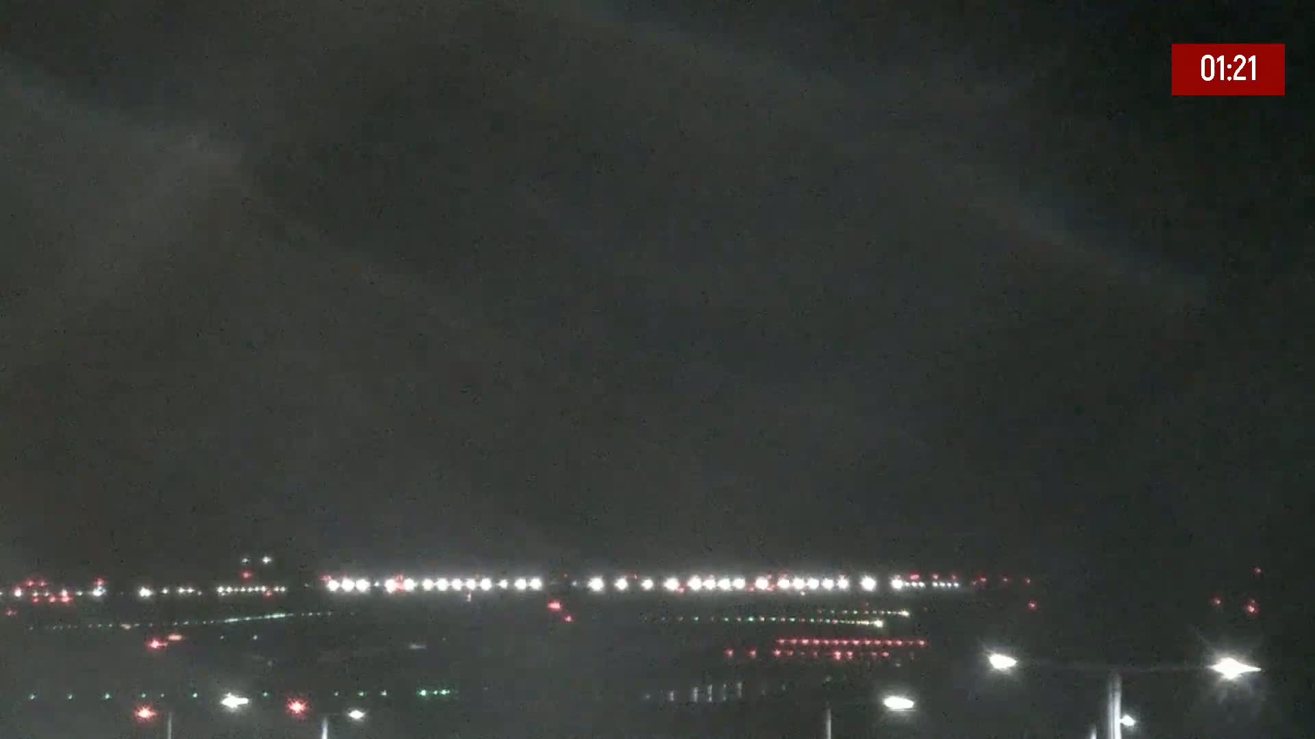 A nighttime long shot of an airport runway with faint lights under a dark, overcast sky.