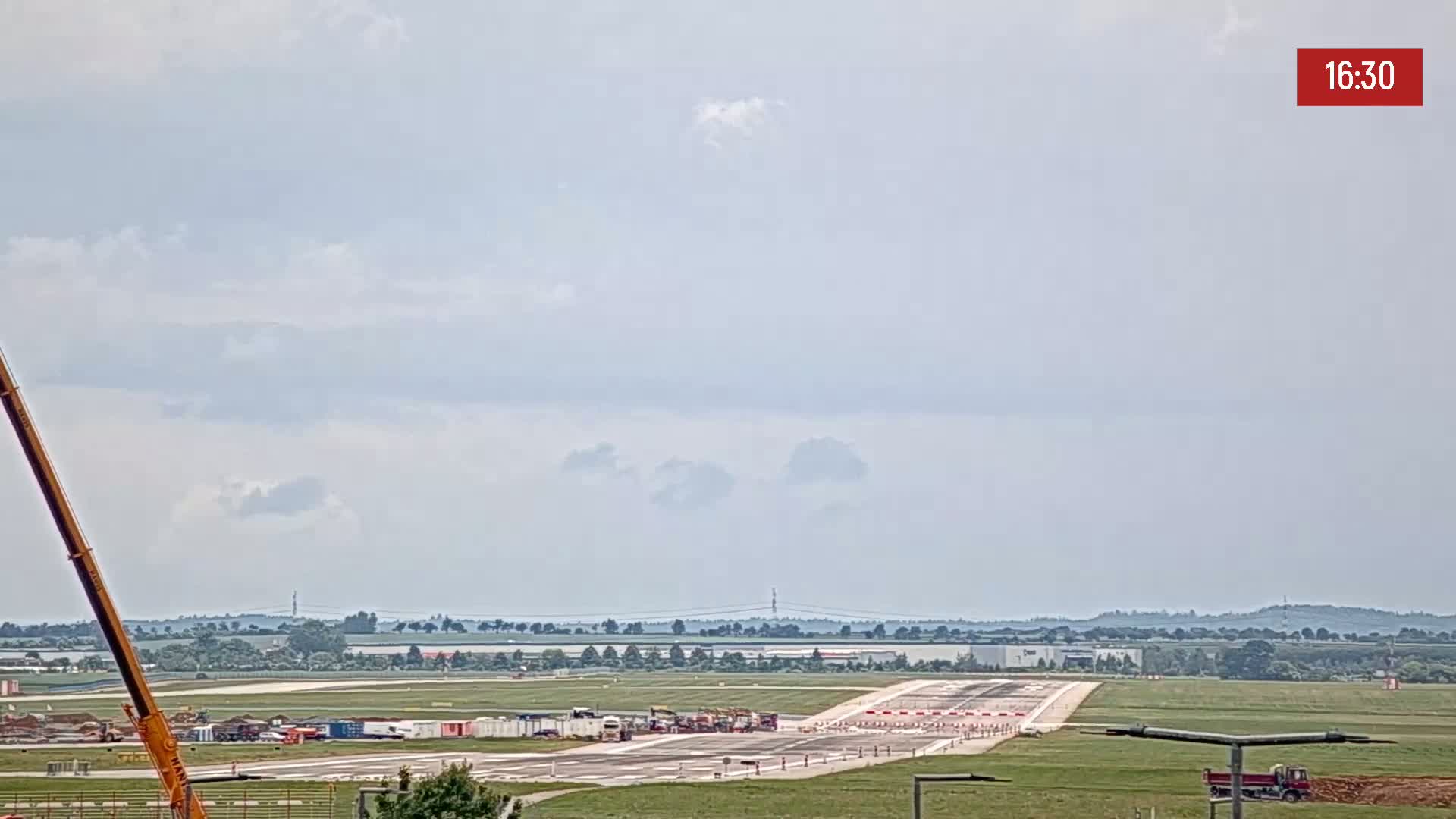 A long runway at an airport is under construction, with several pieces of heavy equipment present on a partly cloudy day.