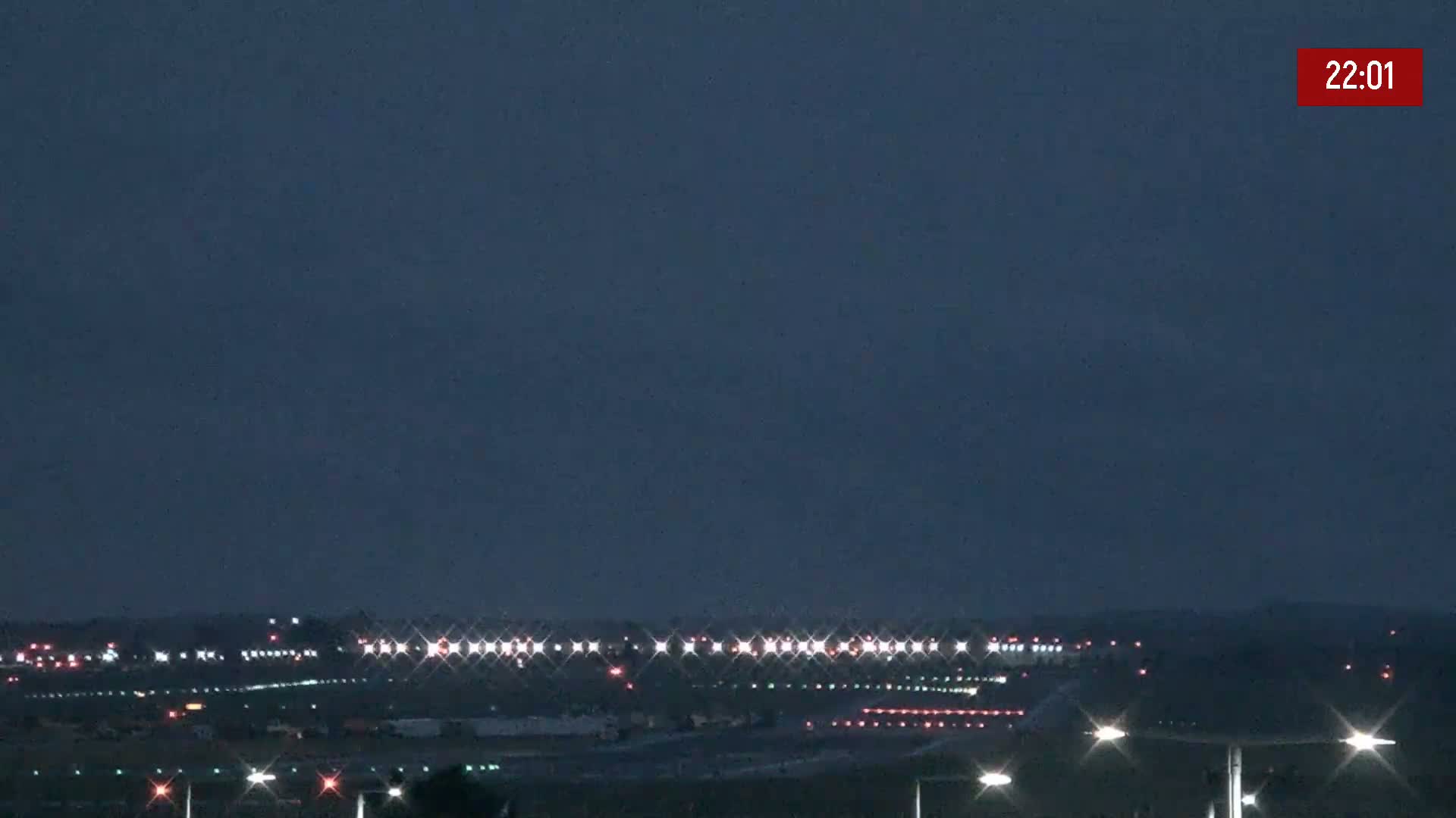 Under a dark night sky, runway lights illuminate a mostly empty airport.